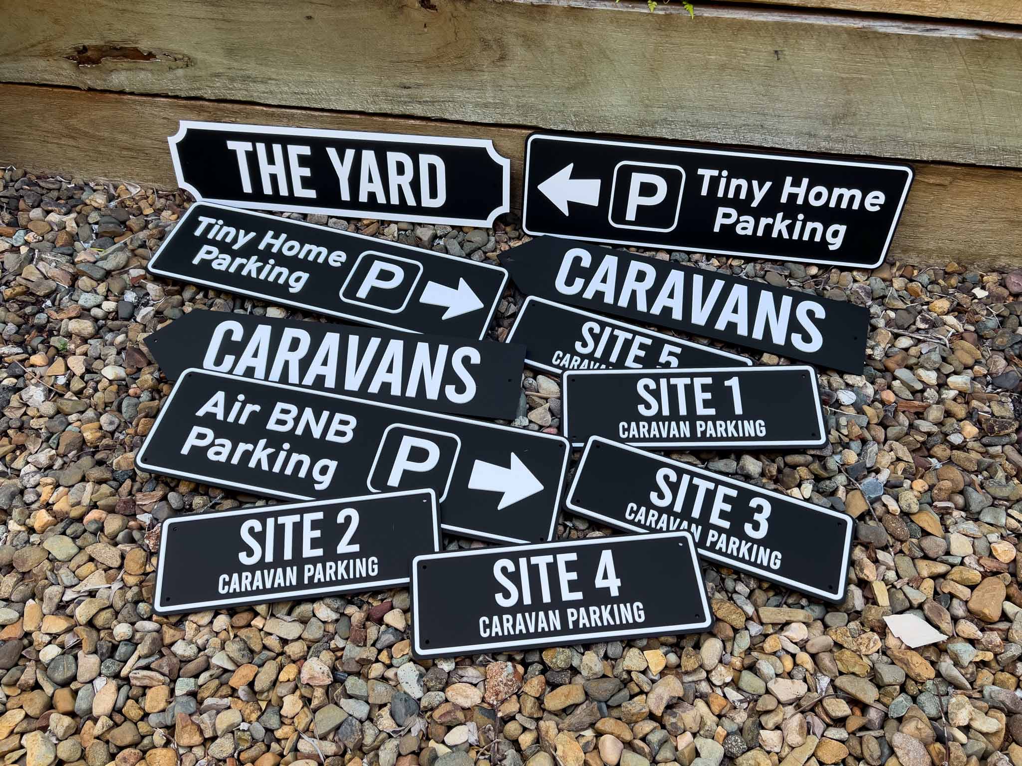 Collection of custom black and white acrylic signage that says 'CARAVANS', 'Tiny Home Parking', 'THE YARD' & 'Site Parking'.