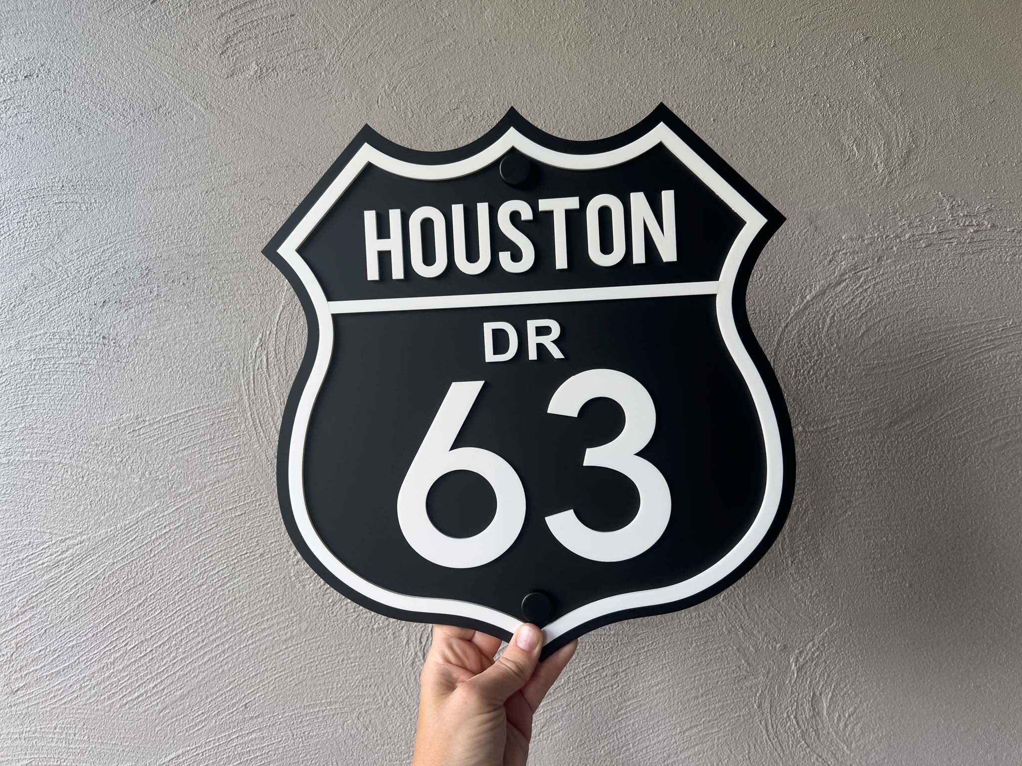 Hand holding a black and white sign with 'HOUSTON DR 63' text against a gray background | Coji Designs