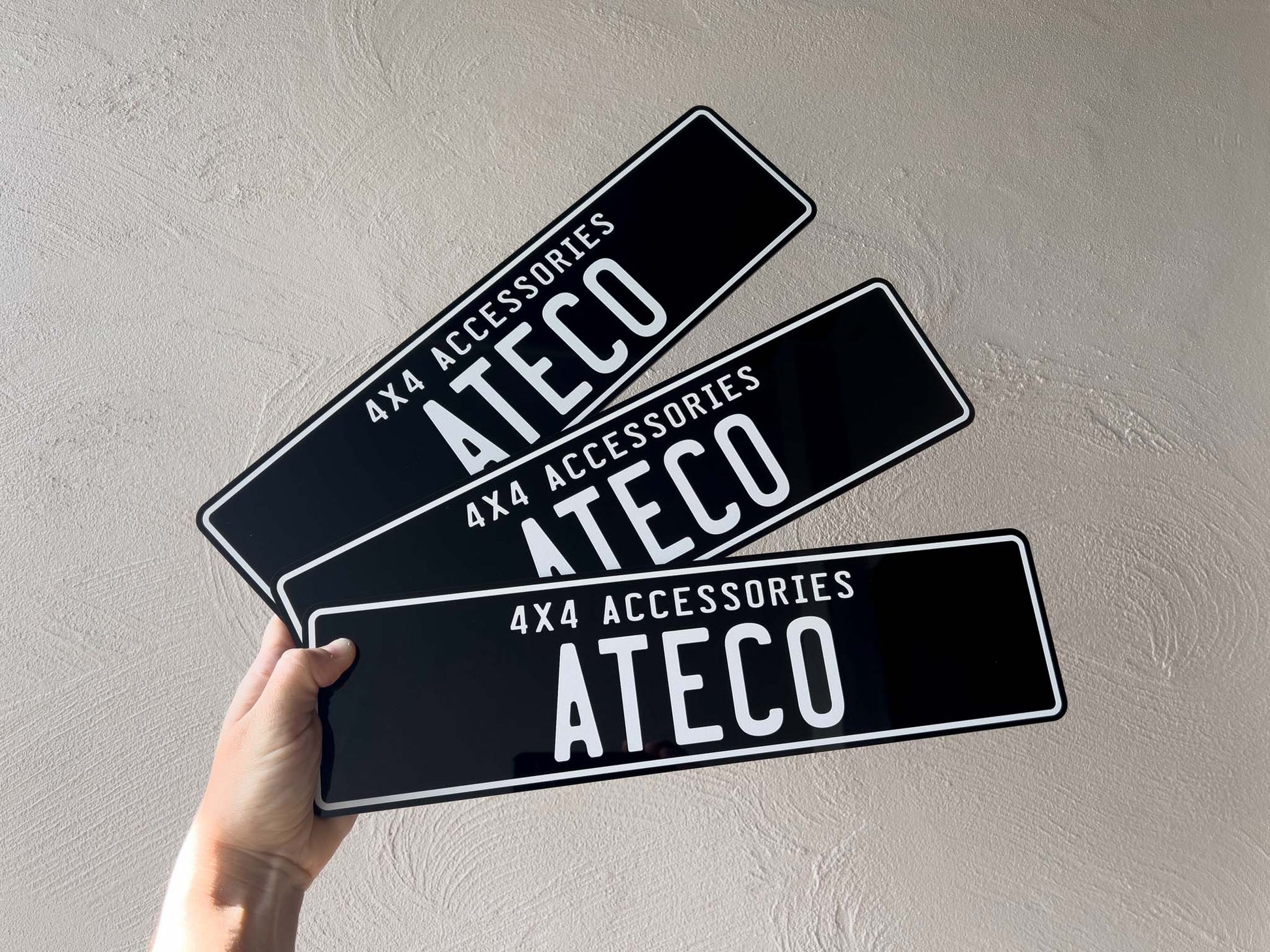 Three ATECO 4x4 accessories custom acrylic plates held against a light grey background