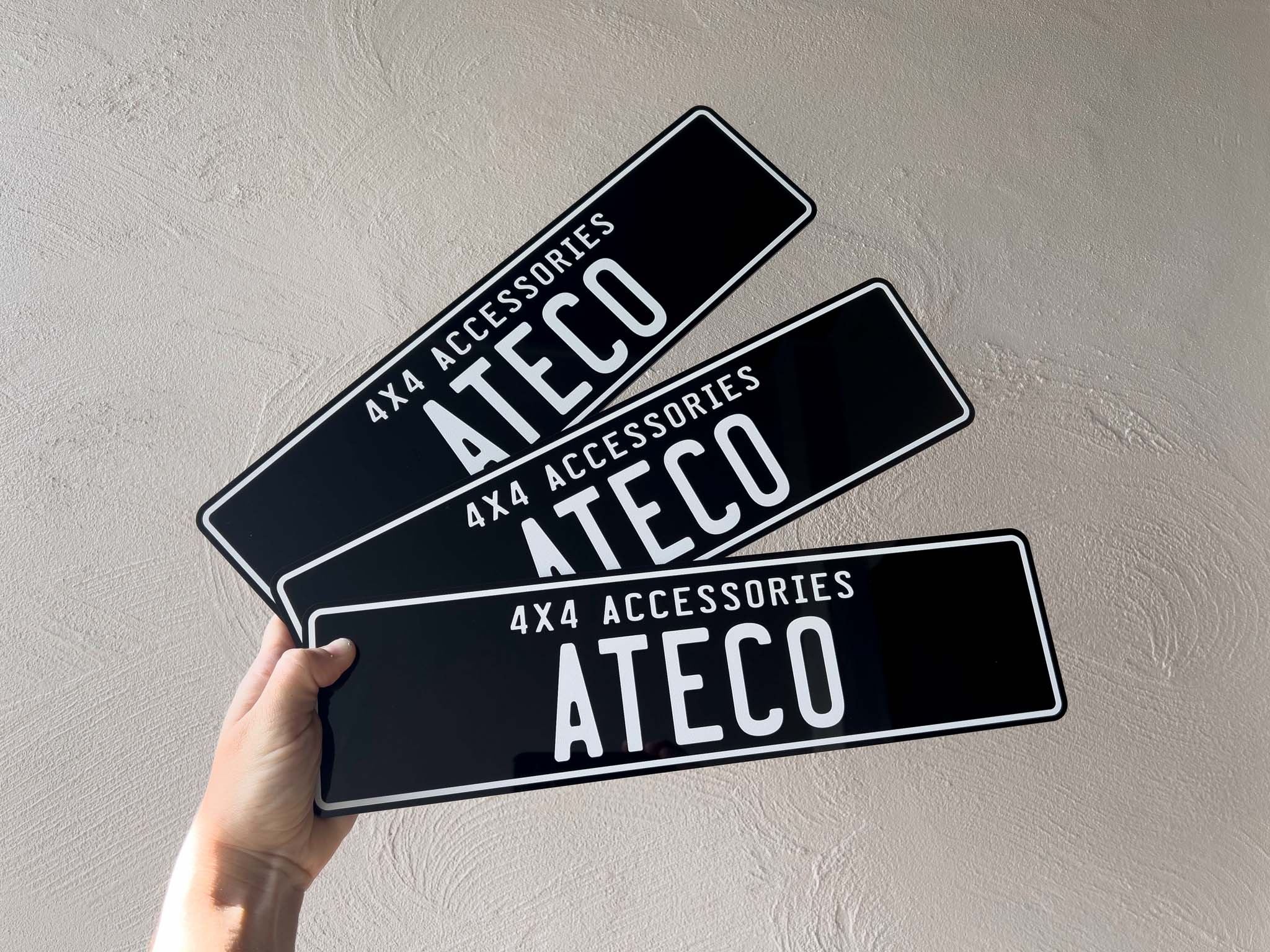 Three ATECO 4x4 accessories custom acrylic plates held against a light grey background