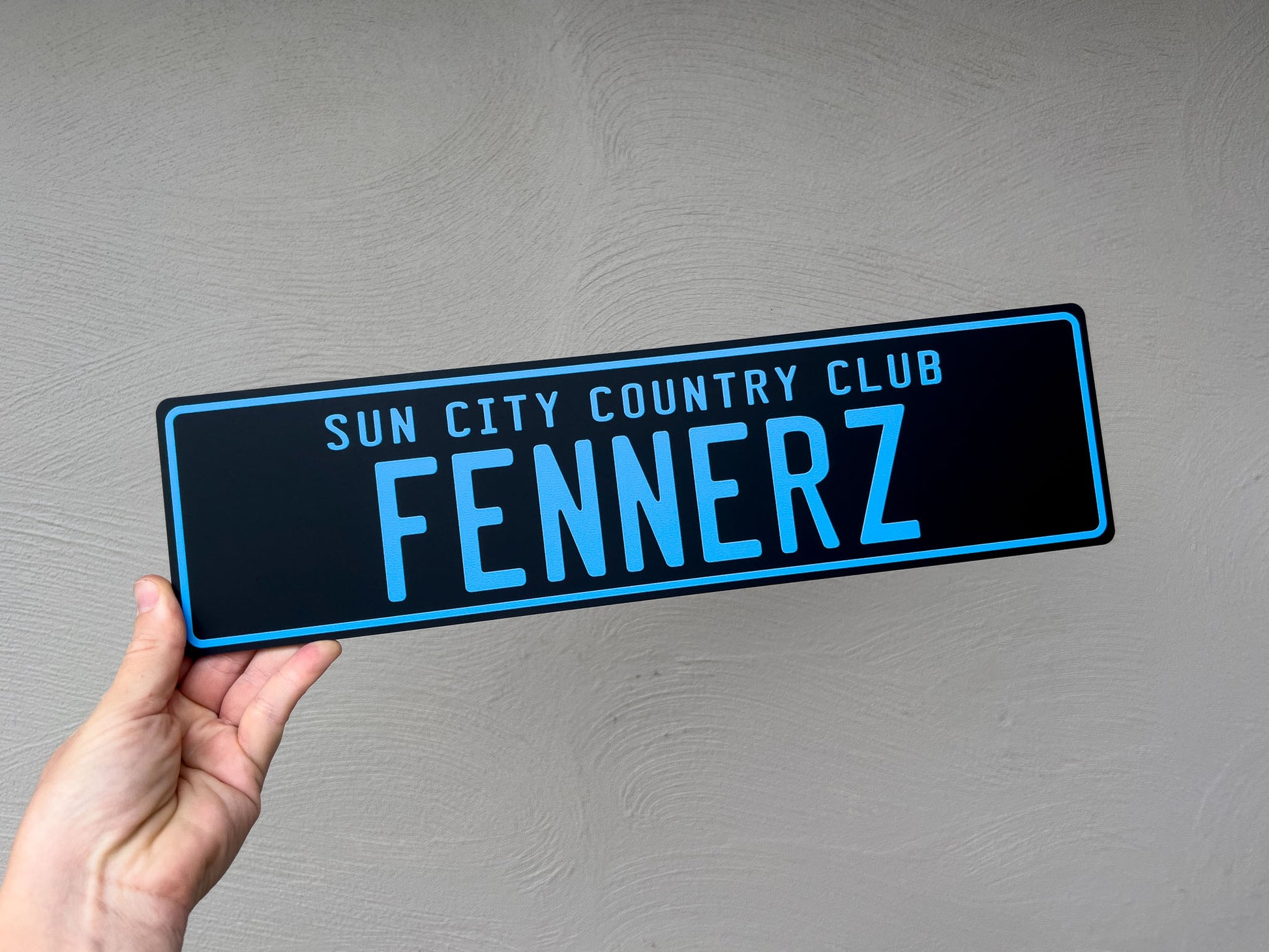 A black slim style novelty acrylic plate with 'Sun City Country Club Fennerz' in blue text against a grey background