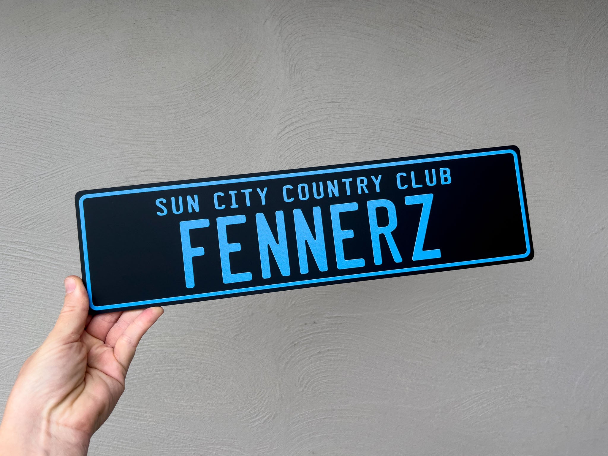 A black slim style novelty acrylic plate with 'Sun City Country Club Fennerz' in blue text against a grey background
