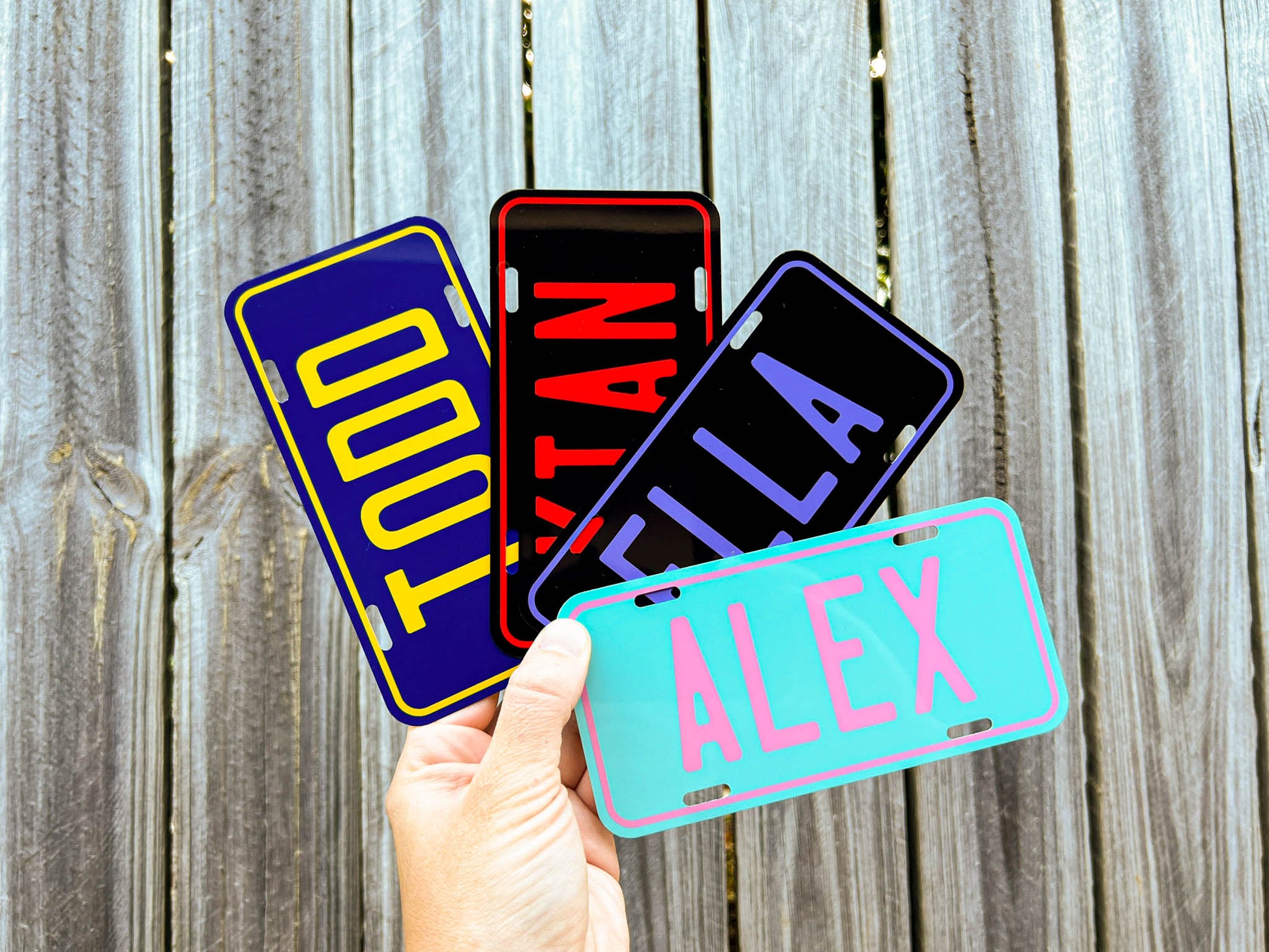 Four colorful metal name plates held by a hand against a wooden background