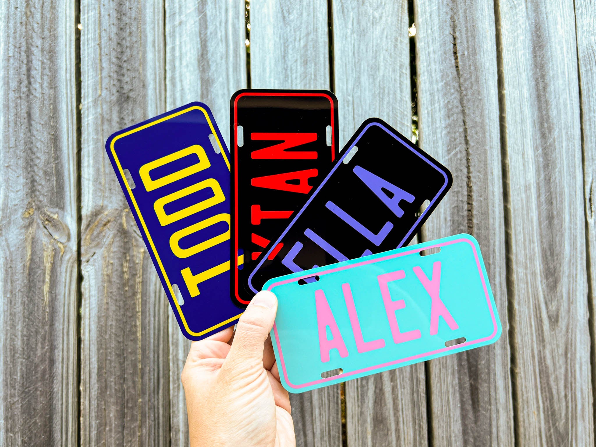 Four colorful metal name plates held by a hand against a wooden background