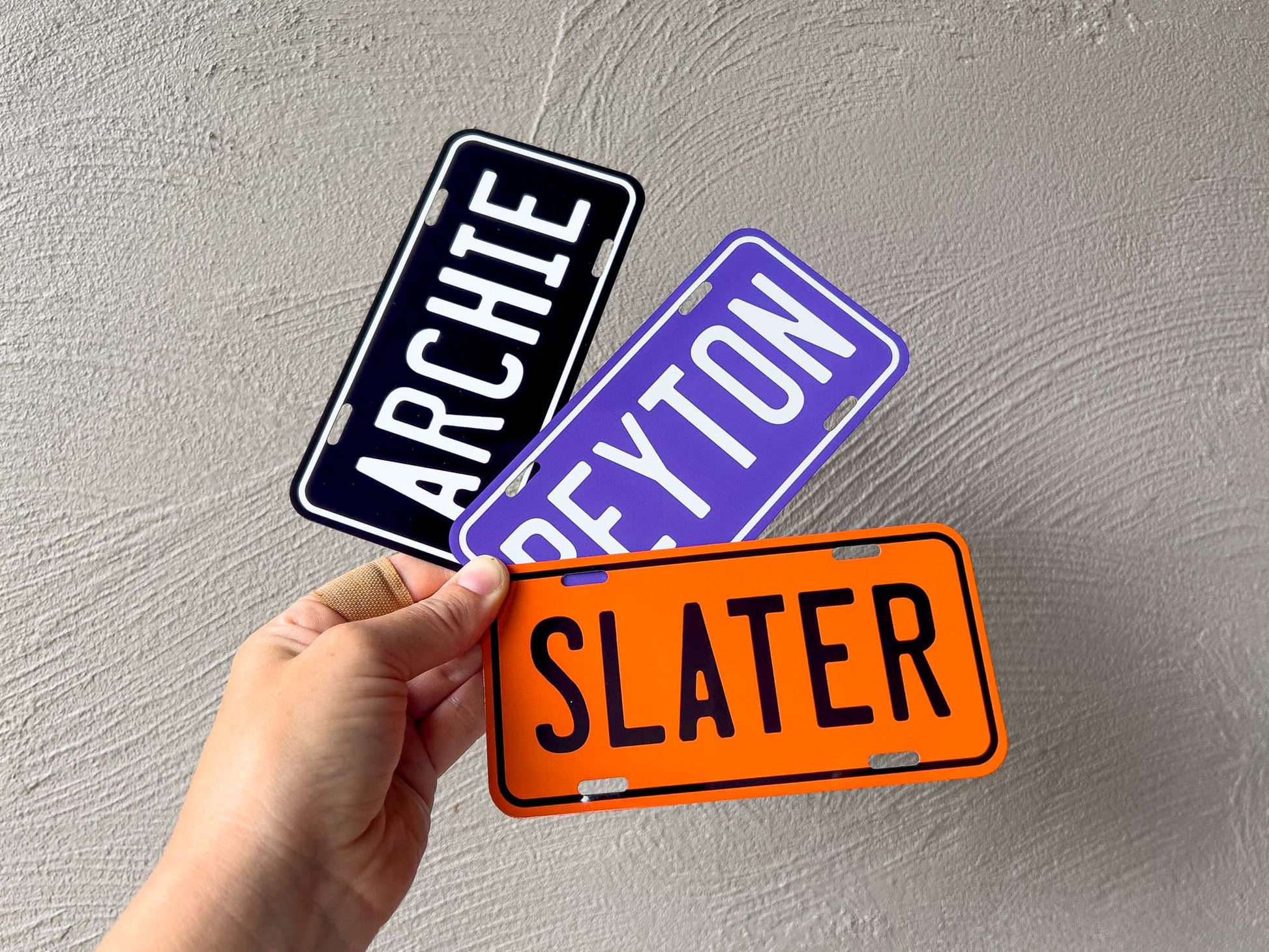 Three name plates labeled 'ARCHIE', 'REYTON', and 'SLATER' held by a hand against a grey background.