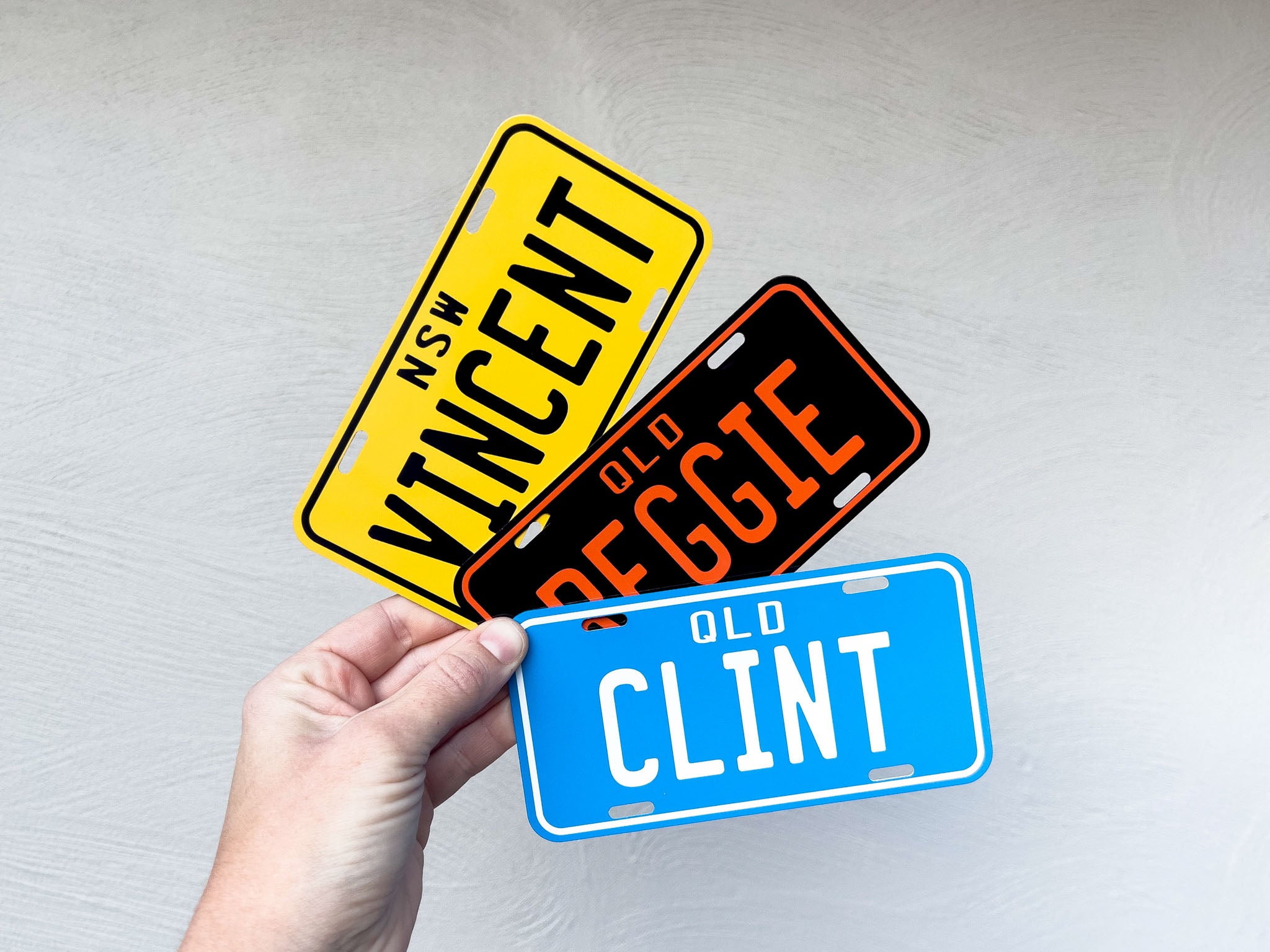Three novelty license plates with names on a plain background