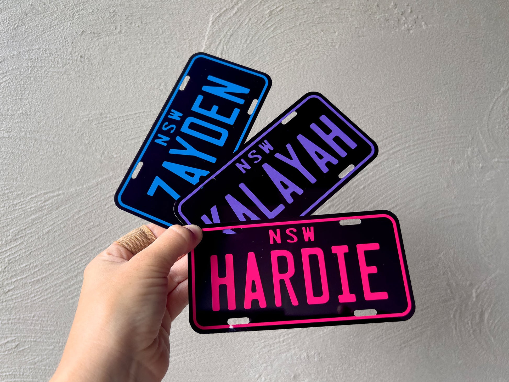 Three personalised mini plates held by a hand against a grey background