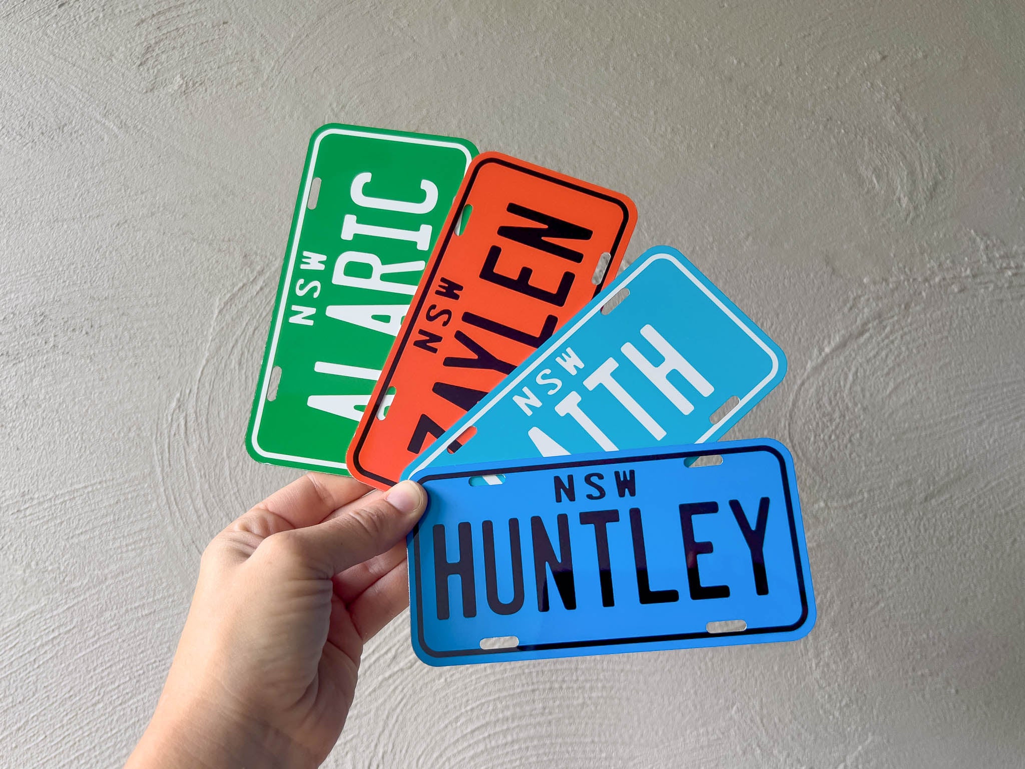 Four colorful number plate designs held by a hand against a light grey background