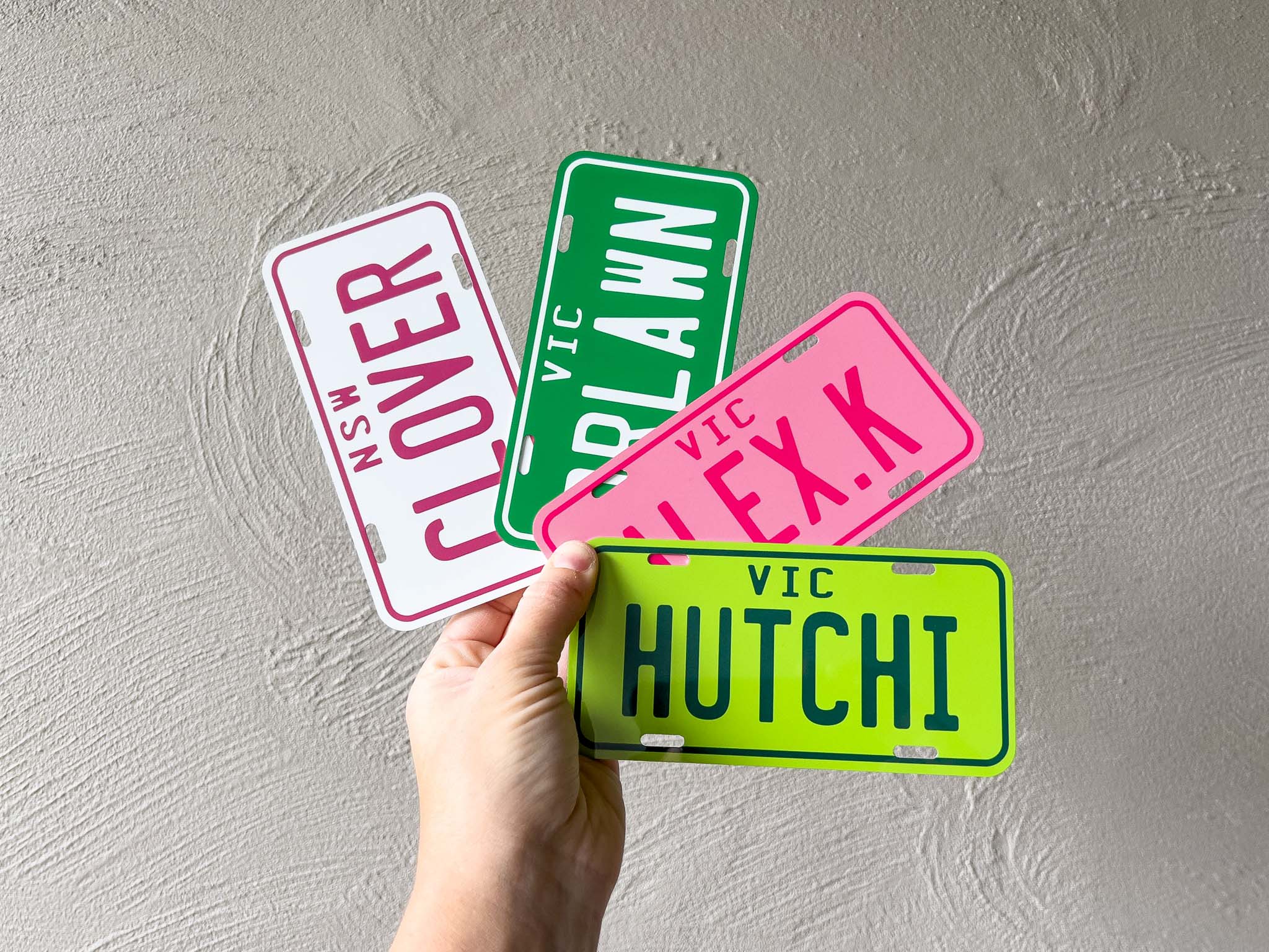 Hand holding four colorful license plate-style signs with text against a grey background