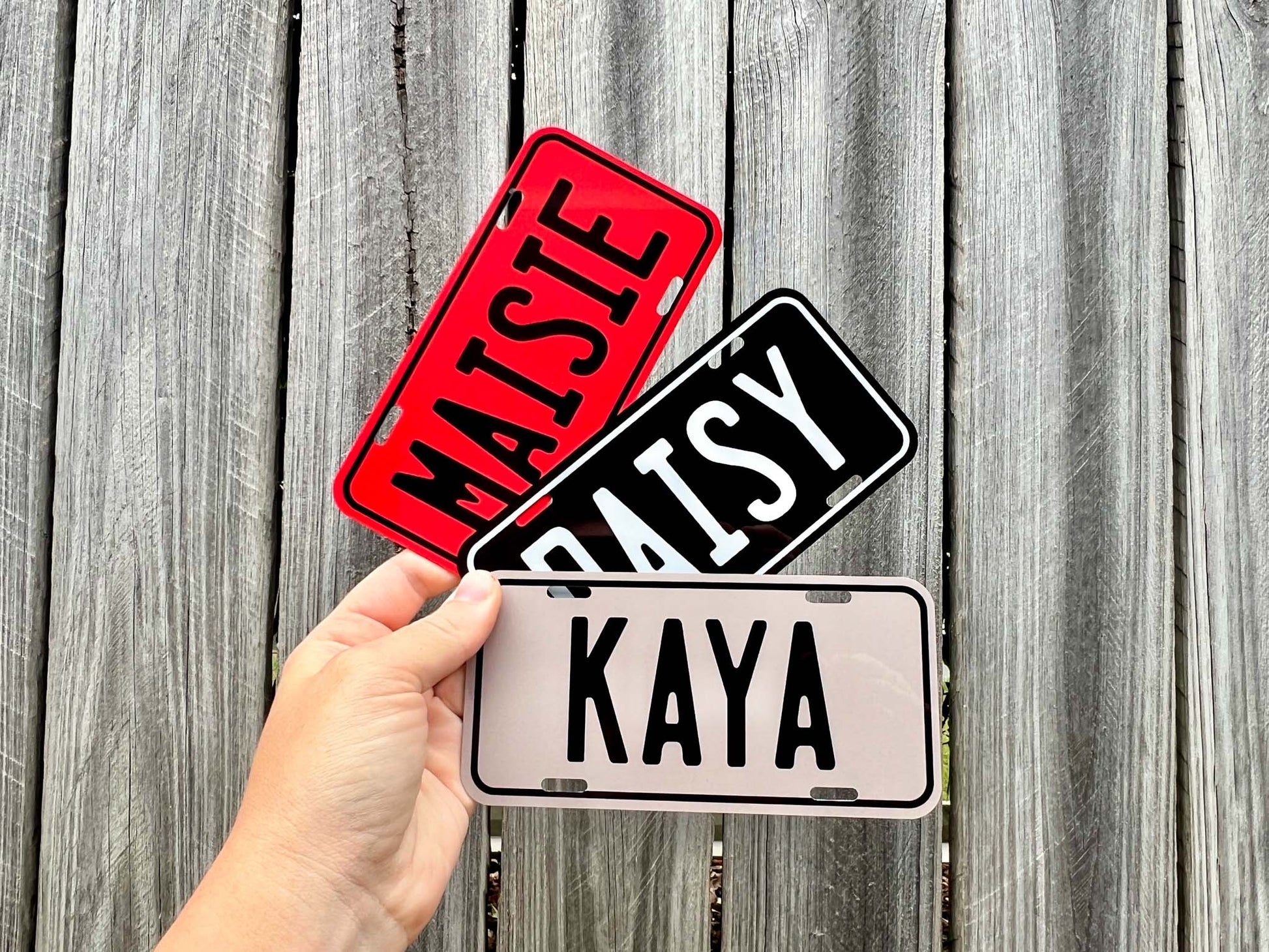 Three name plates labeled 'MAISTE', 'DAISY', and 'KAYA' held against a wooden background.