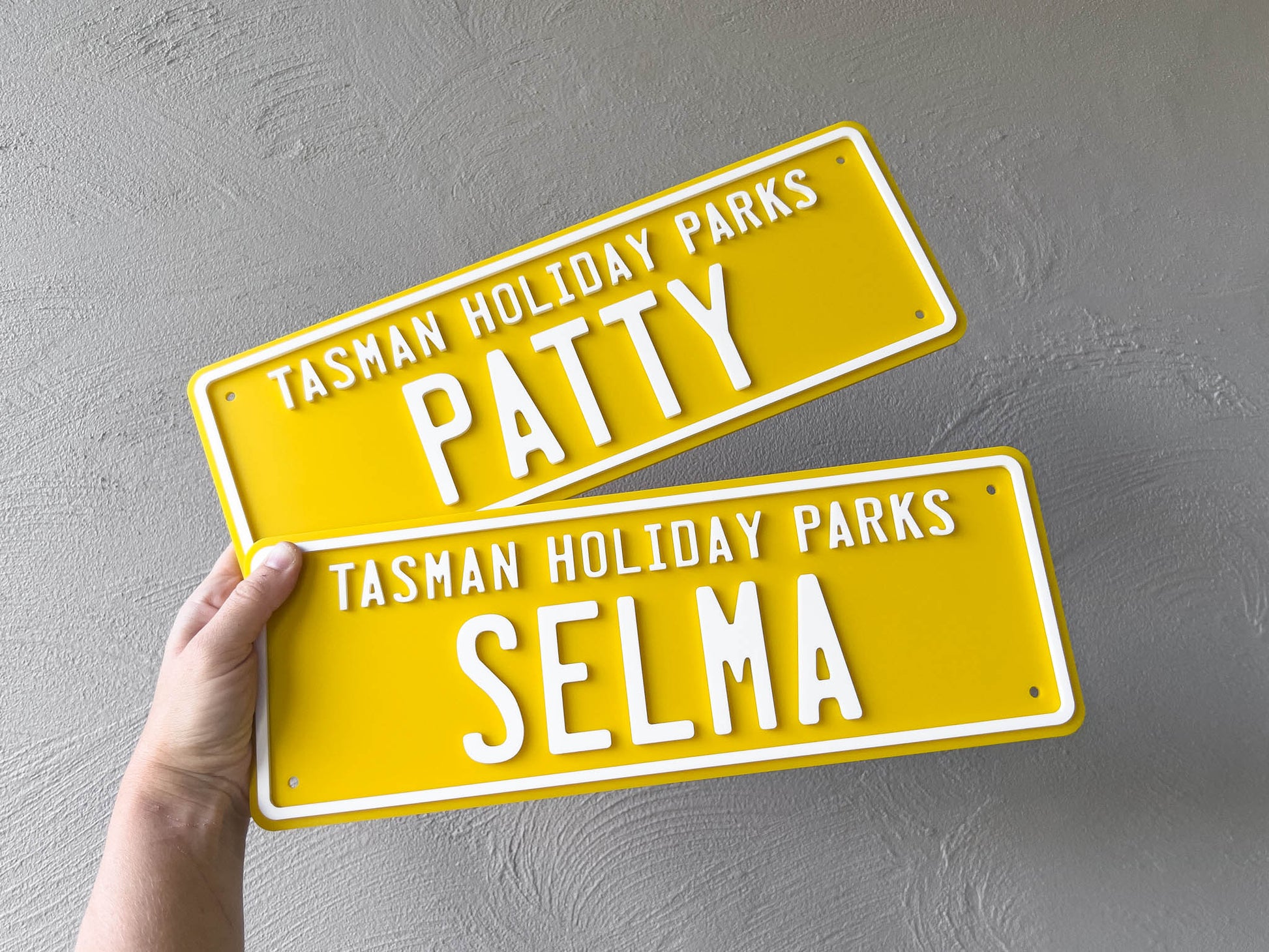 Two custom outdoor acrylic cover plates in yellow and white that read 'Tasman Holiday Parks' with the names 'Patty' & 'Selma'.