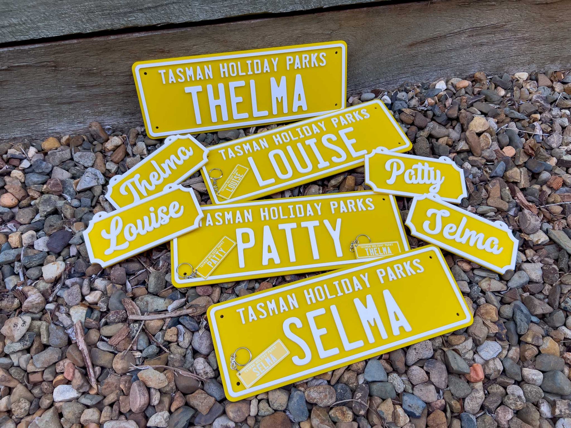 A collection of sunshine yellow and white acrylic plates for 'Tasman Holiday Parks' with custom names and metal aluminium keychains.