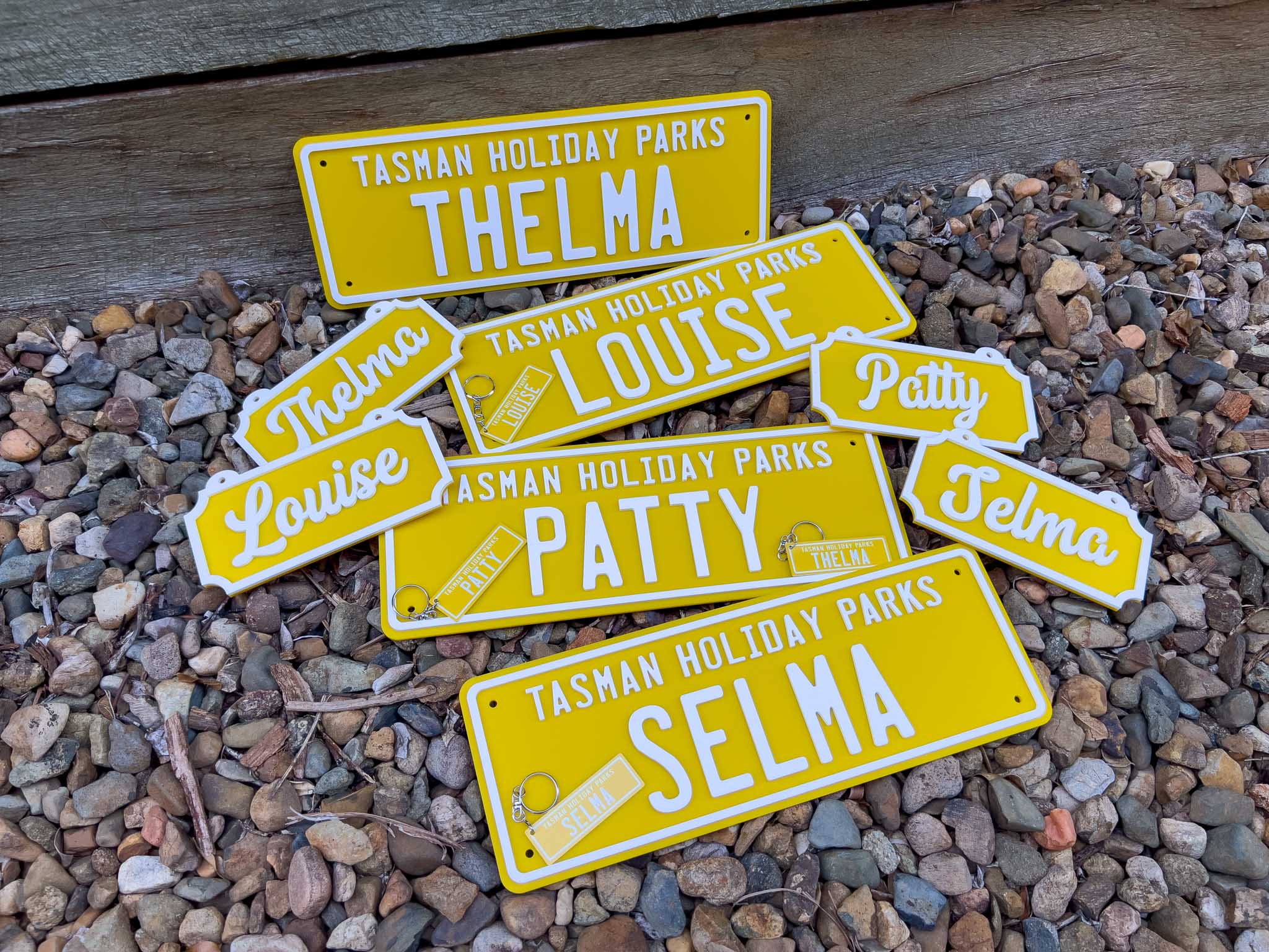 A collection of sunshine yellow and white acrylic plates for 'Tasman Holiday Parks' with custom names and metal aluminium keychains.