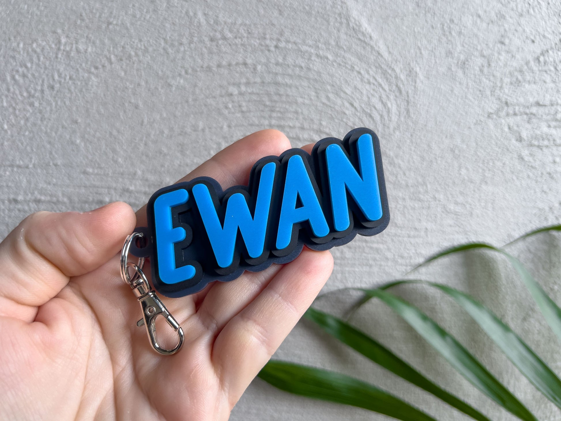 Keychain with 'EWAN' letters held in a hand against a neutral background