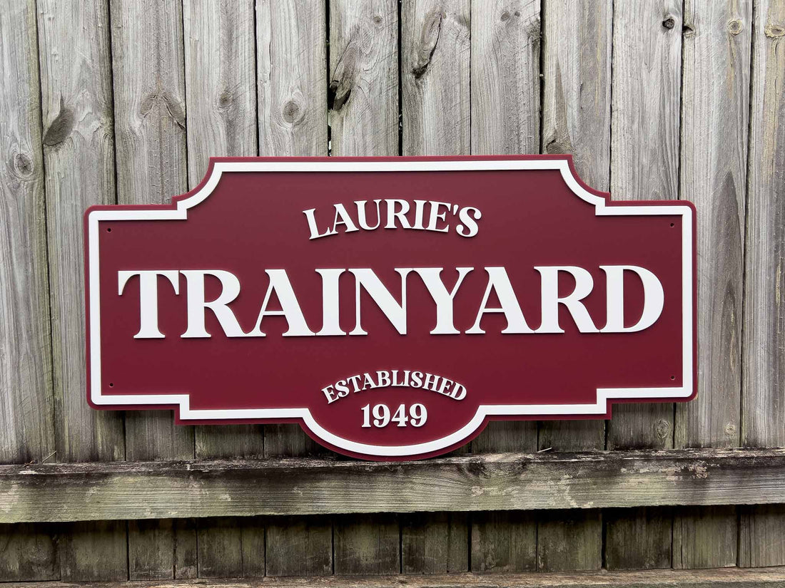 Handcrafted acrylic maroon and white sign with 'Laurie's Trainyard' on a wooden background.
