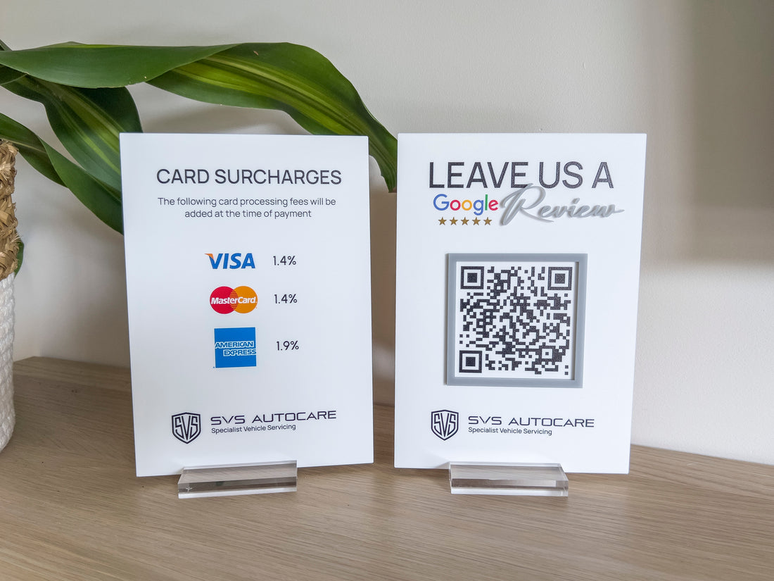 Two table displays signs for 'SVS Autocare', one with card surcharges and the other with a QR code Google review sign.