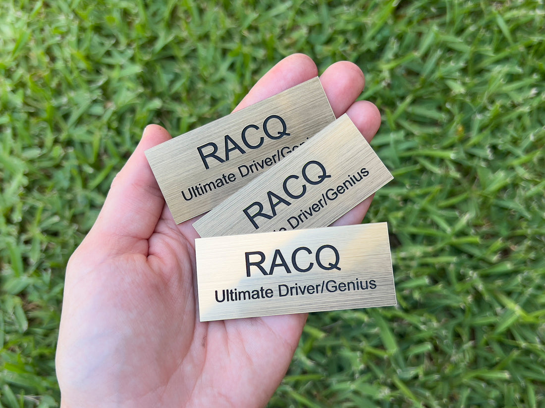 Three brushed gold engraved trophy plaques that read 'RACQ Ultimate Driver/Genius'.