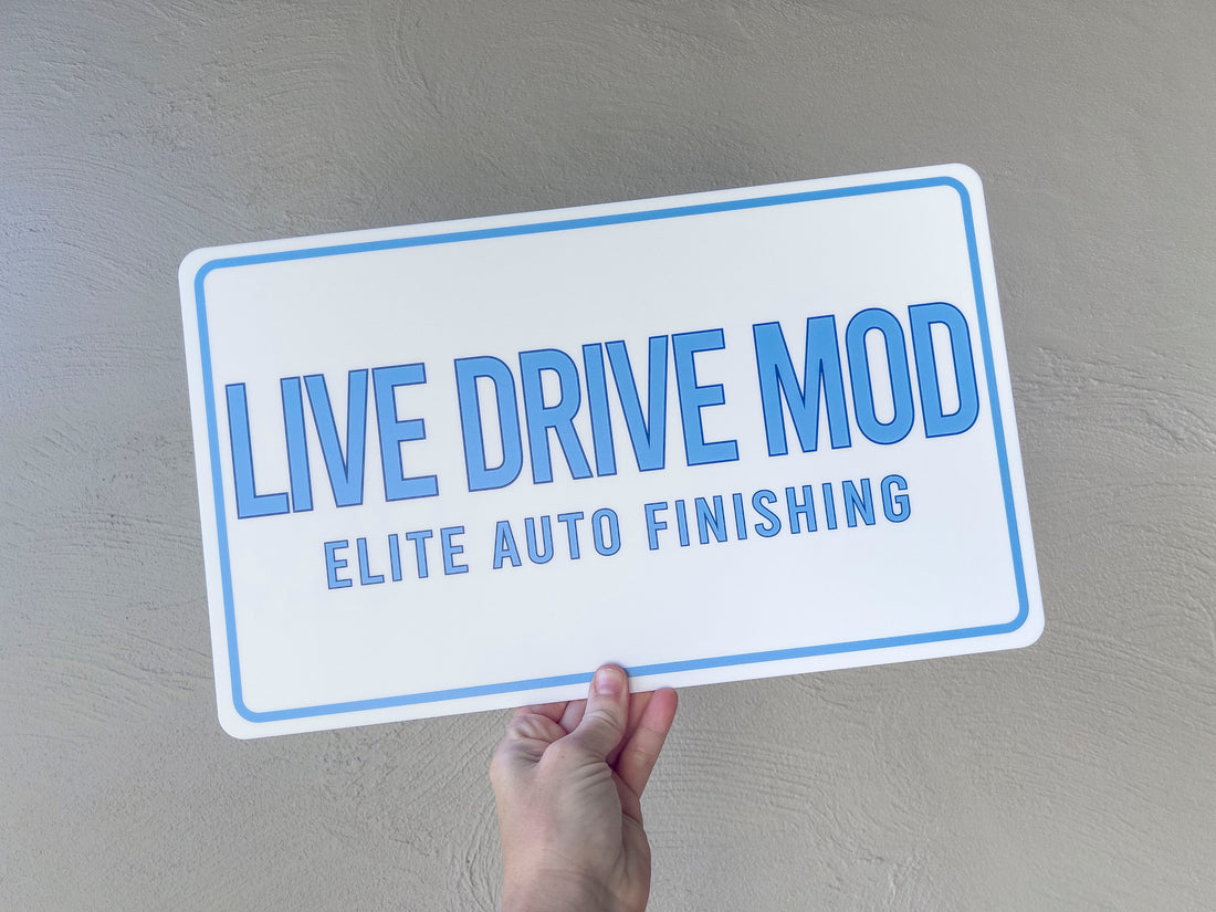 Hand holding a sign that reads 'LIVE DRIVE MOD ELITE AUTO FINISHING' against a gray background