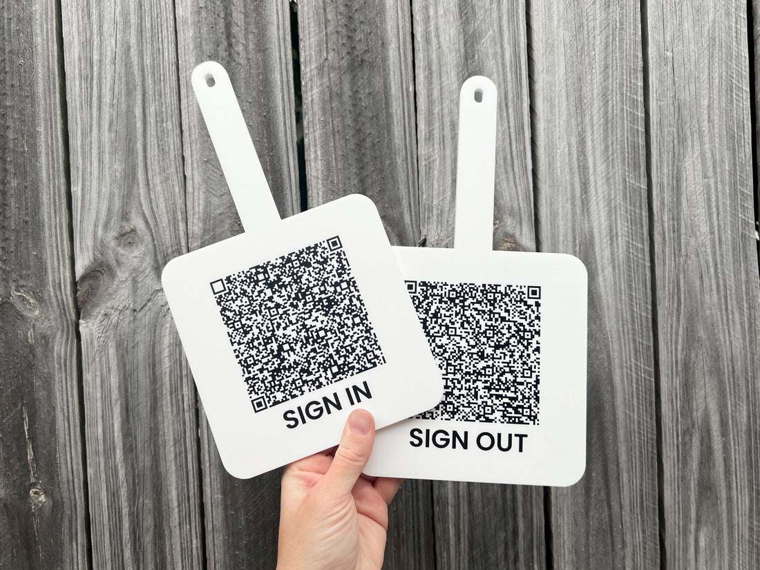 Two signs with QR codes labeled 'SIGN IN' and 'SIGN OUT' held against a wooden background.