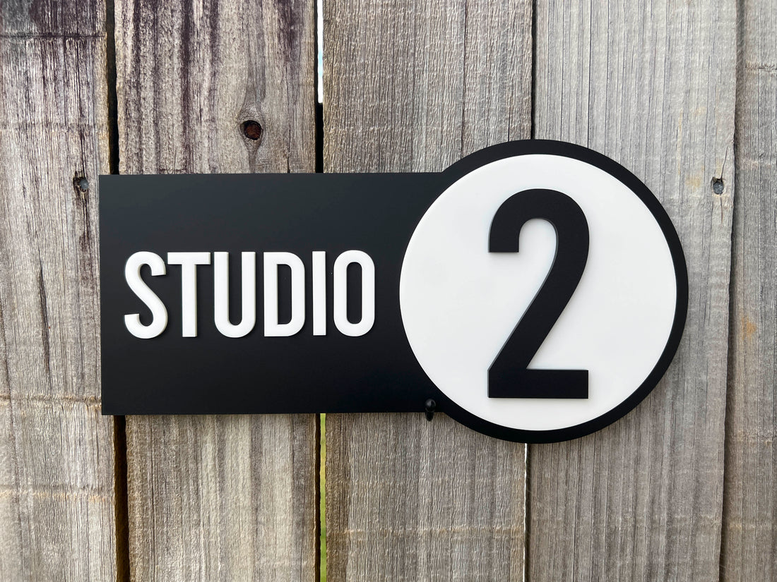 Black and white door sign with 'STUDIO 2' on a wooden background