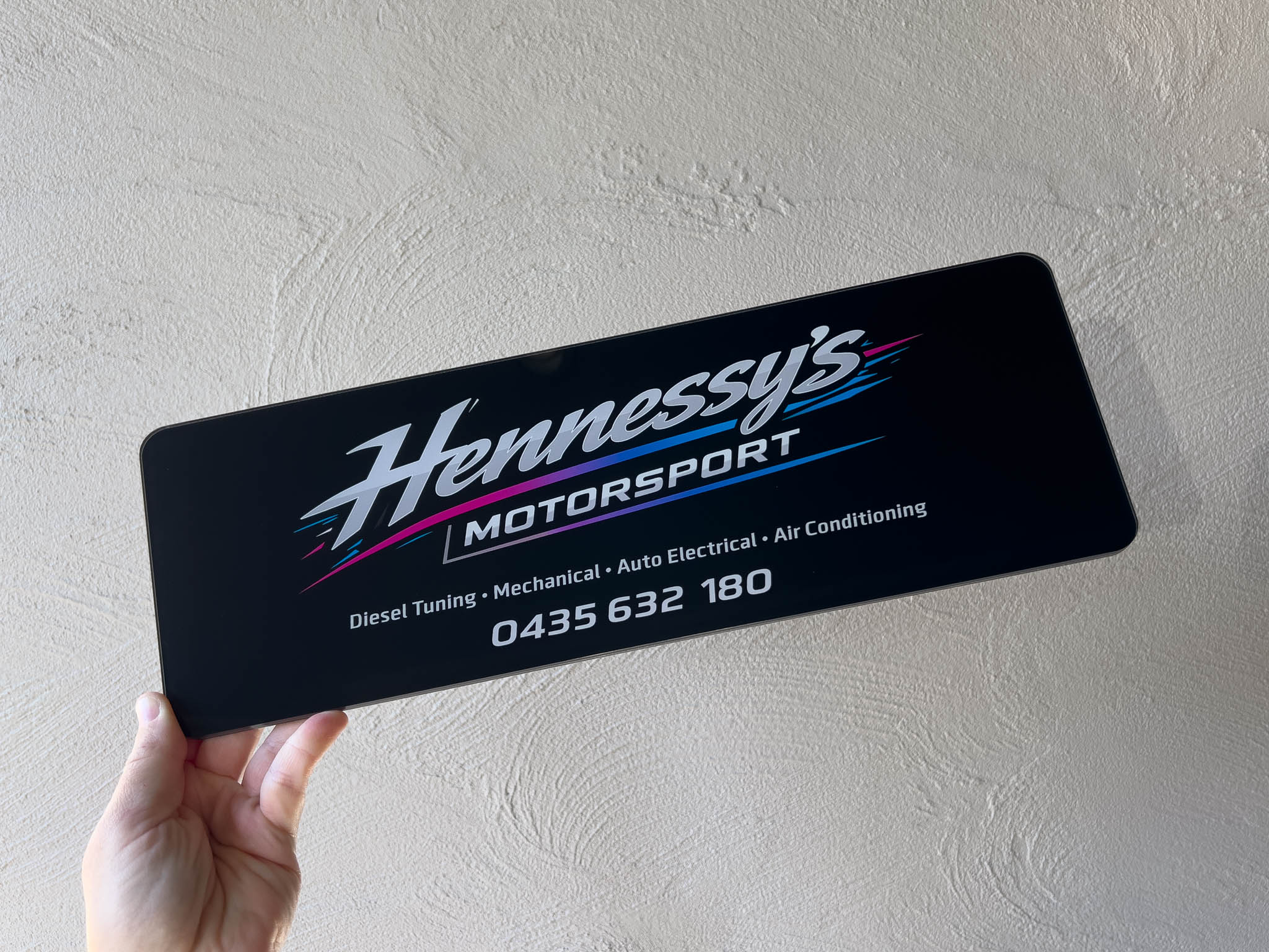 A personalised branded logo plate that reads 'Hennessy's Motorsport' in a high glossy finish with white and vibrant colours on a black background.