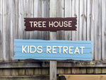 A ship wreakage style plank sign with custom text that reads 'TREE HOUSE' & 'KIDS RETREAT' in a dark brown and blue colour.
