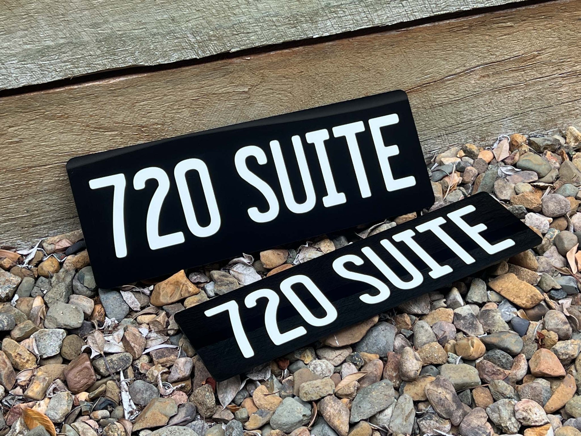 Two black number plate signs with '720 SUITE' text on a wooden surface and pebbles.
