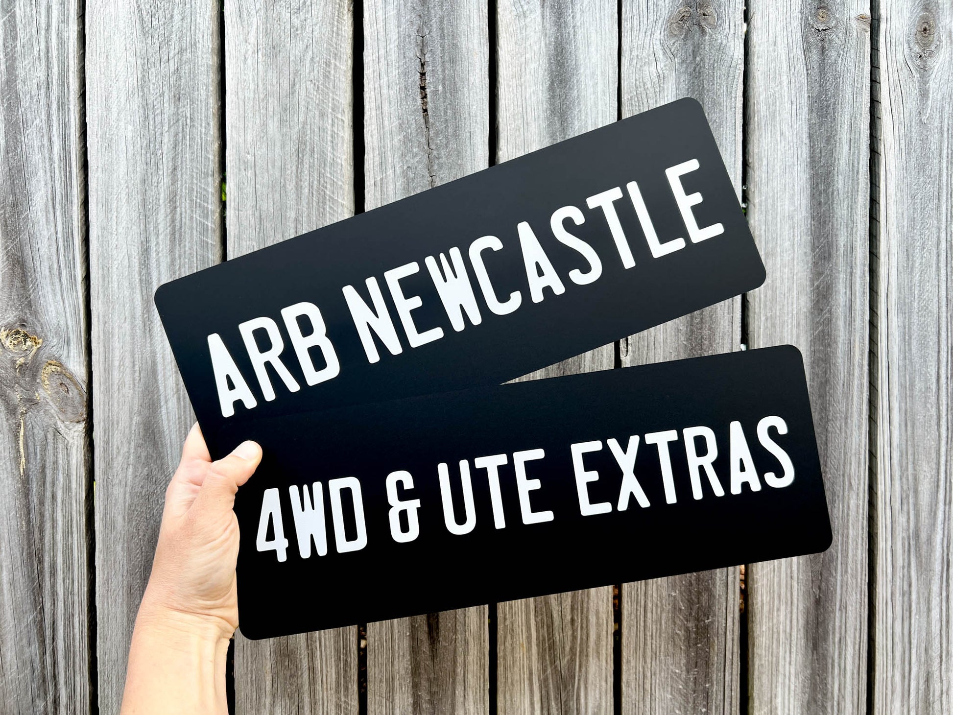 Two matte black acrylic plates that read 'ARB NEWCASTLE' & '4WD & UTE EXTRAS' in white text.