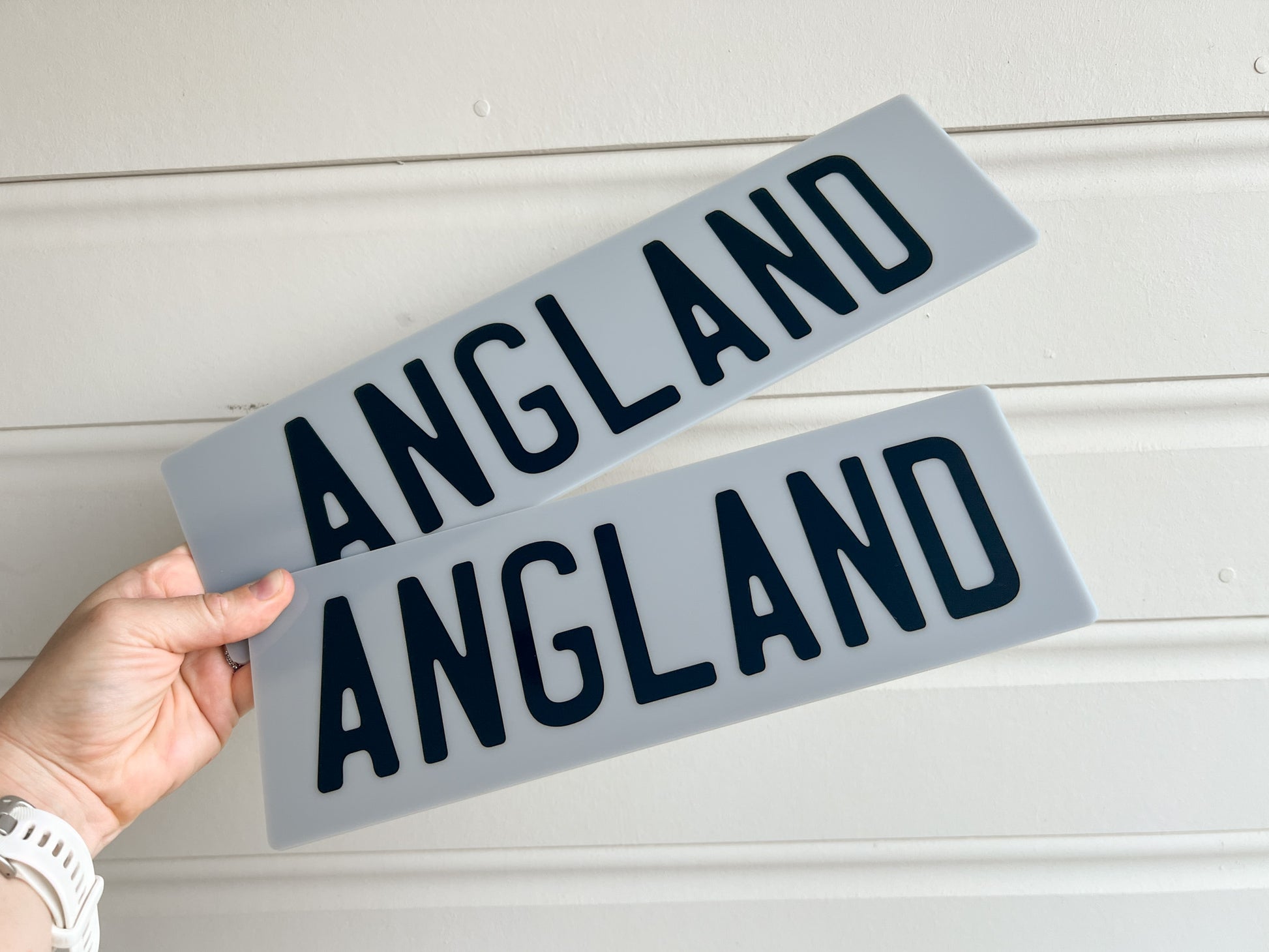 Two grey acrylic plates with the text 'ANGLAND' printed in black text.