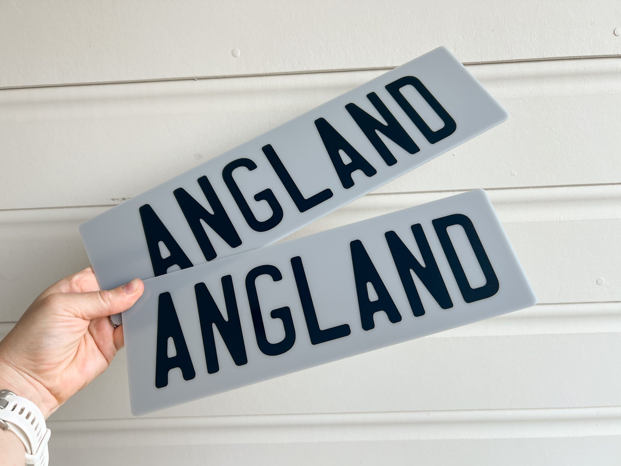 Two grey acrylic plates with the text 'ANGLAND' printed in black text.
