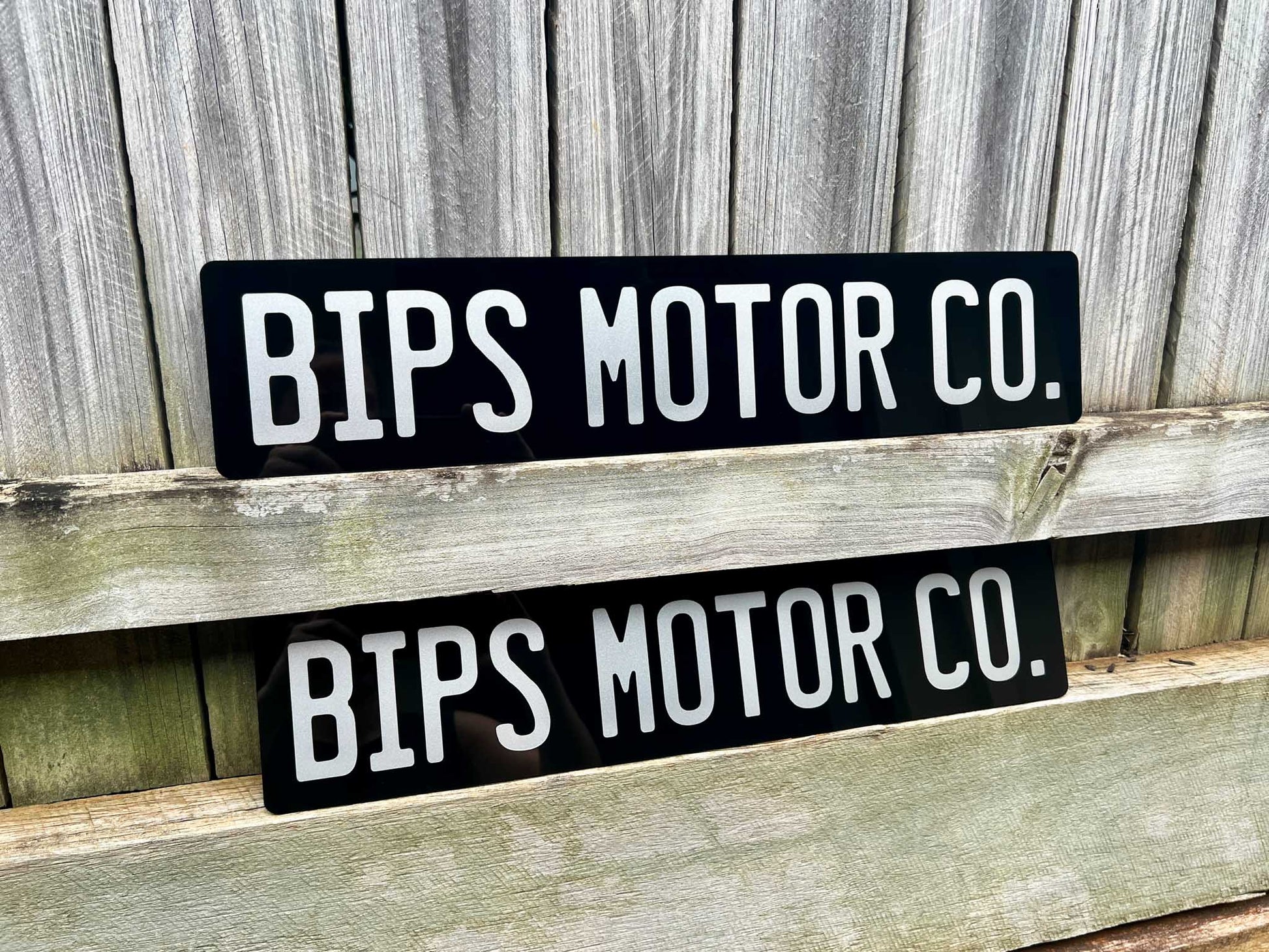 Two black and white 'BIPS MOTOR CO.' Euro acrylic signs on a wooden surface with a wooden background.