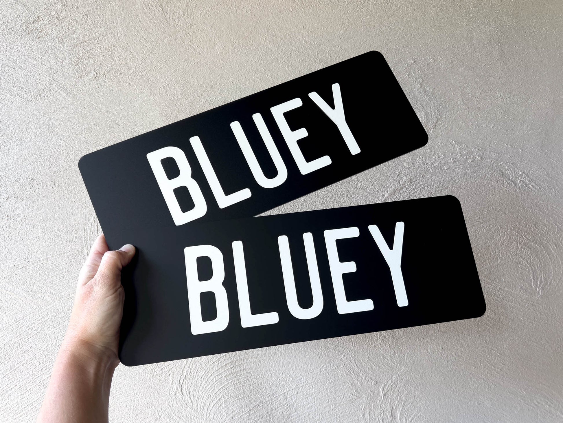 Two black matte acrylic plates with the text 'BLUEY' printed in white ink