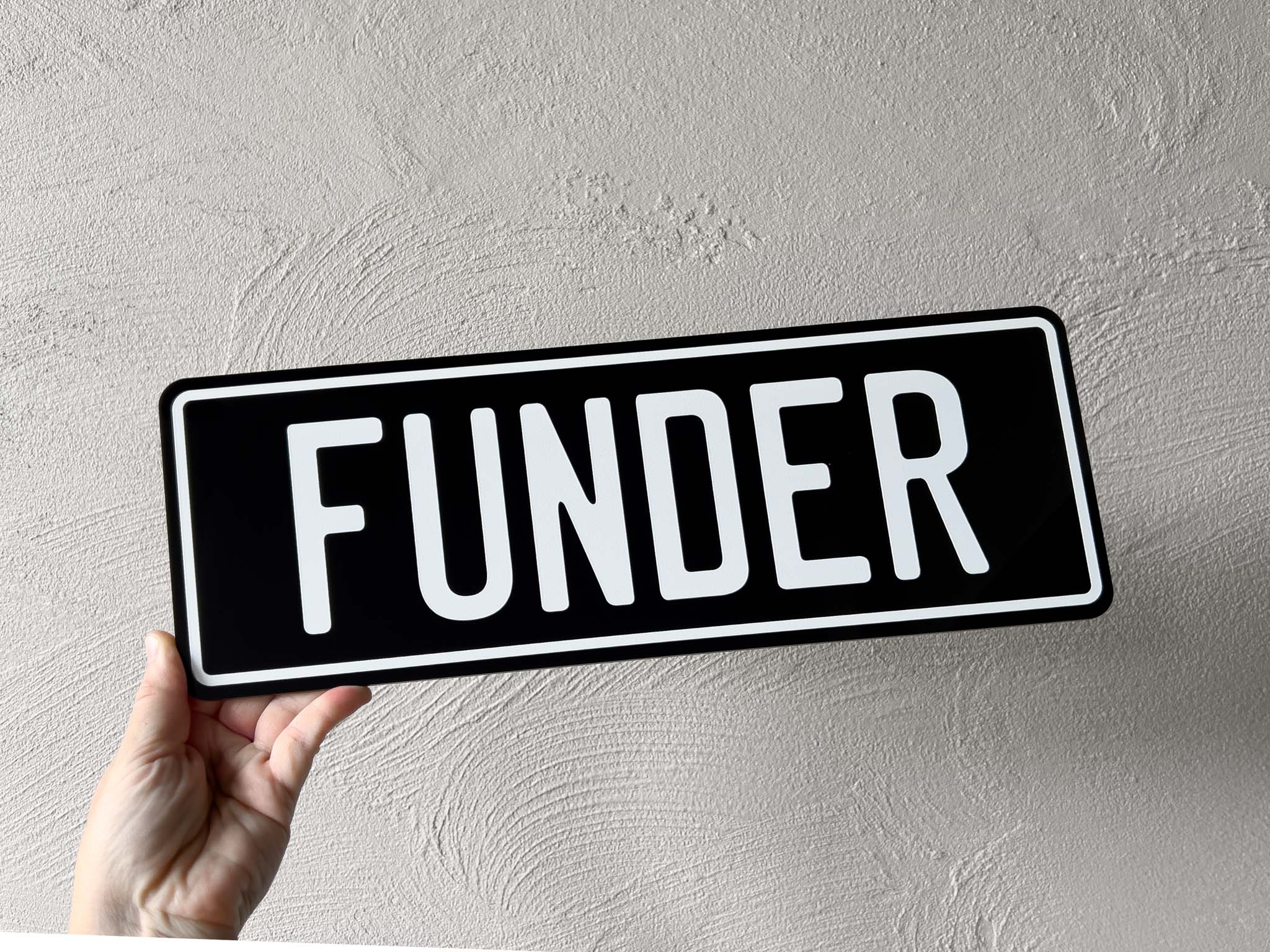 Hand holding a custom printed black and white custom printed acrylic plate that reads 'FUNDER'.