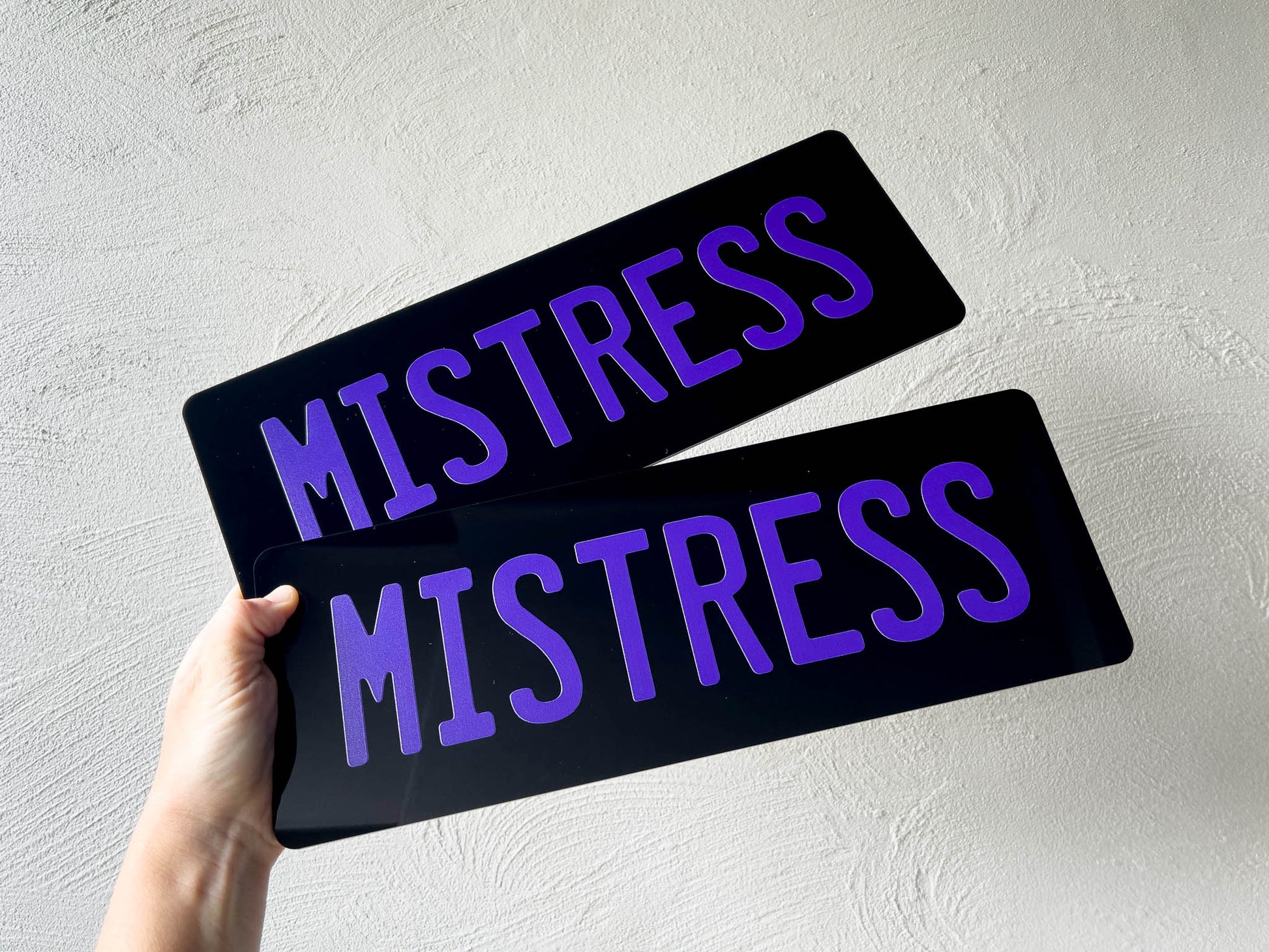 Two black plates with 'MISTRESS' in purple text held against a light grey background.