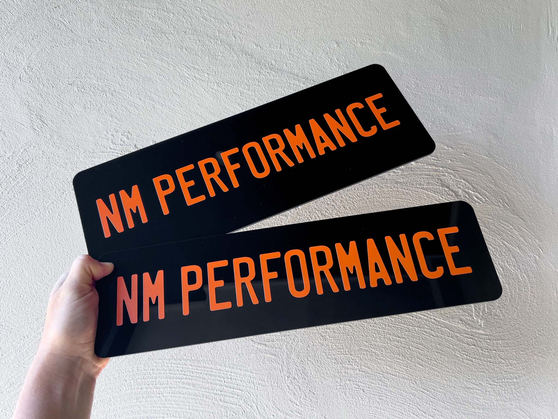 Two glossy black plates with printed orange text that reads 'NM PERFORMANCE'.
