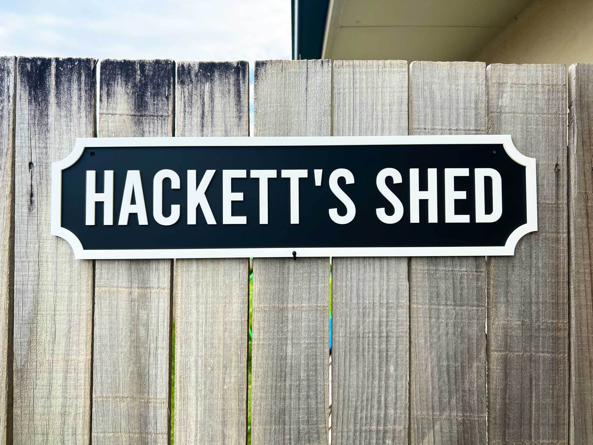 Wooden sign with 'HACKETT'S SHED' text on a wooden fence.