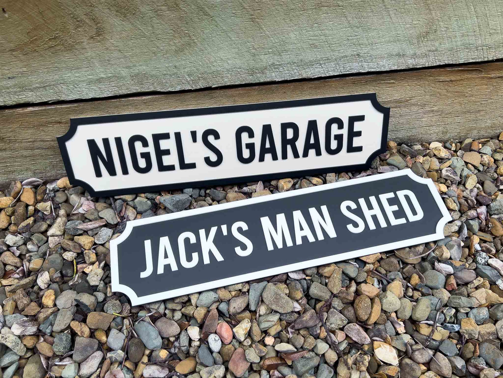 Two decorative signs for 'Nigel's Garage' and 'Jack's Man Shed' on a pebble surface.