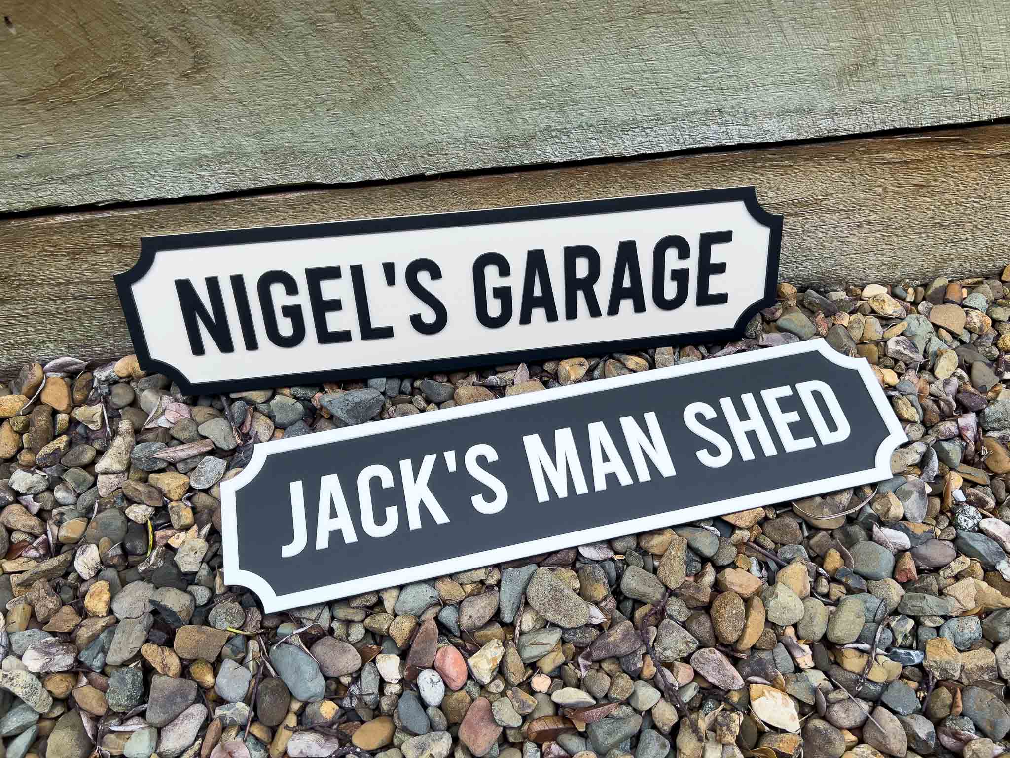 Two decorative signs for 'Nigel's Garage' and 'Jack's Man Shed' on a pebble surface.
