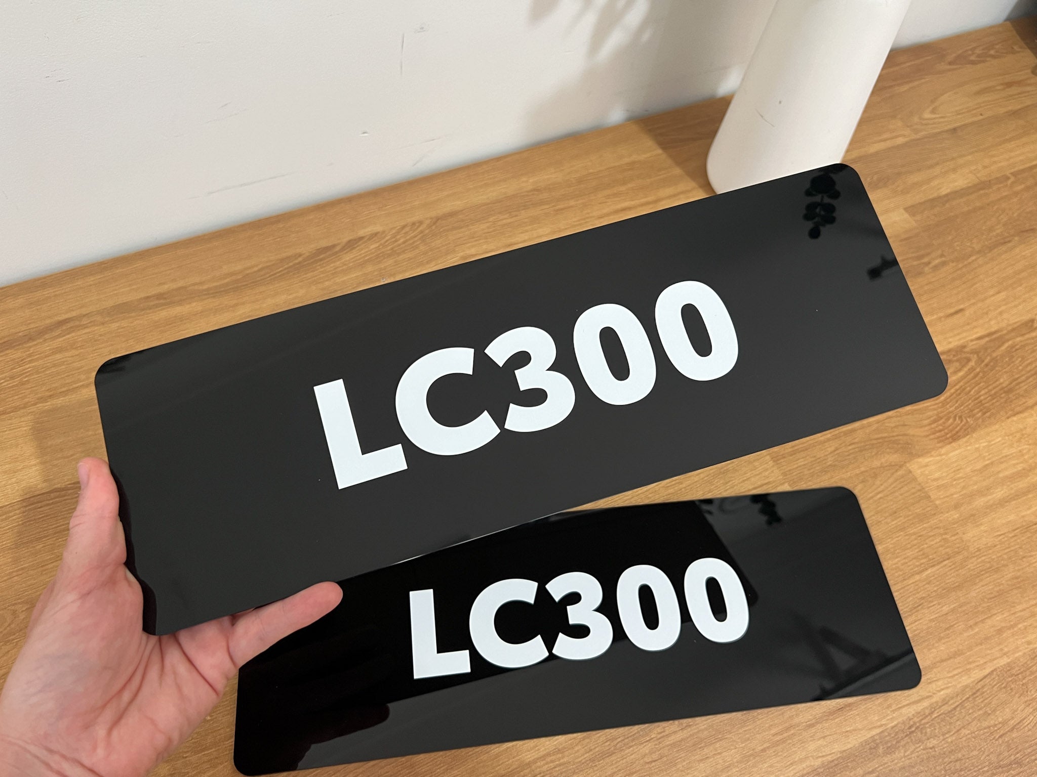 Two black gloss cover plates with 'LC300' text held by a hand on a wooden surface.
