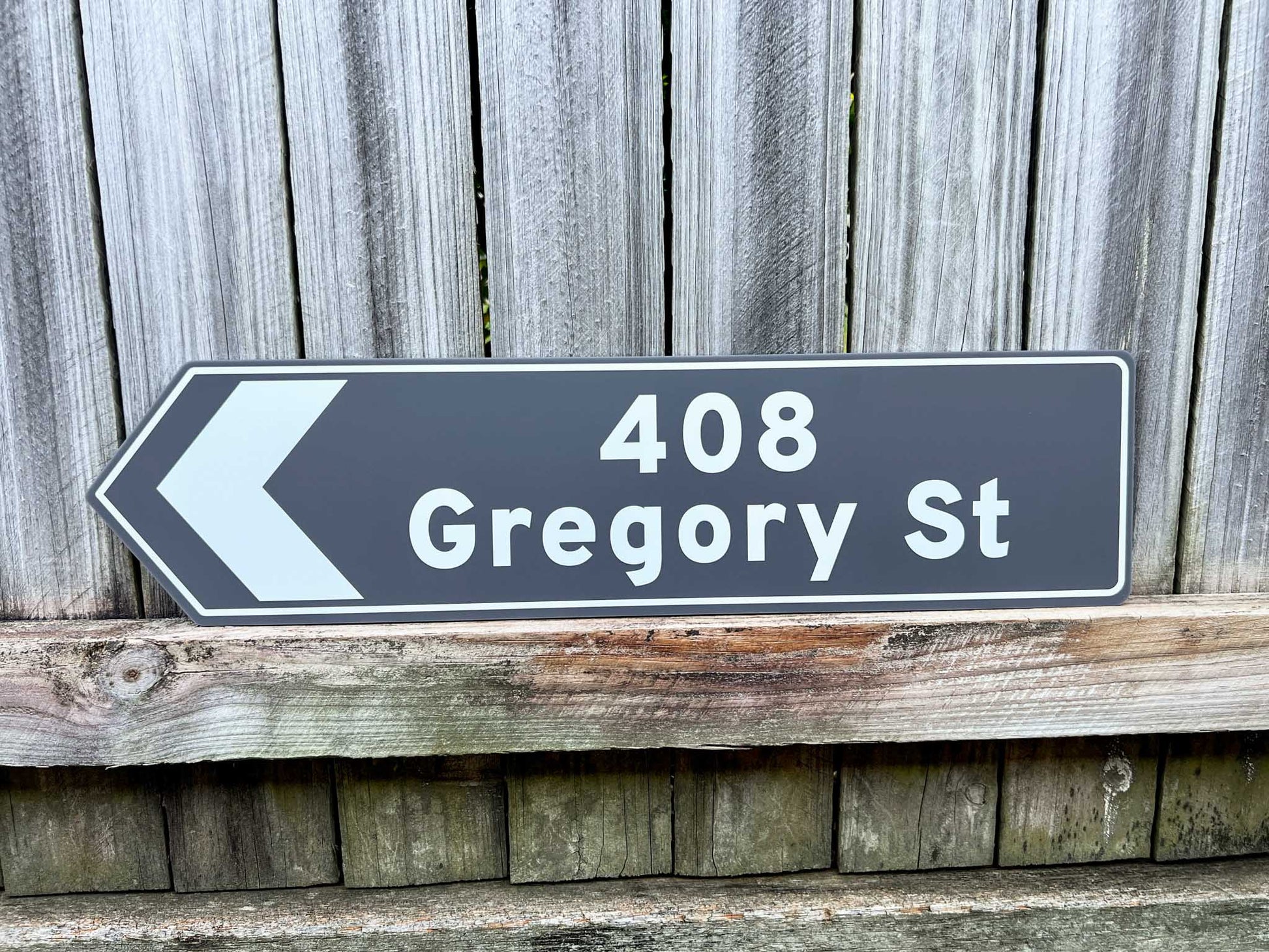 Street sign pointing to 408 Gregory St against a wooden fence background
