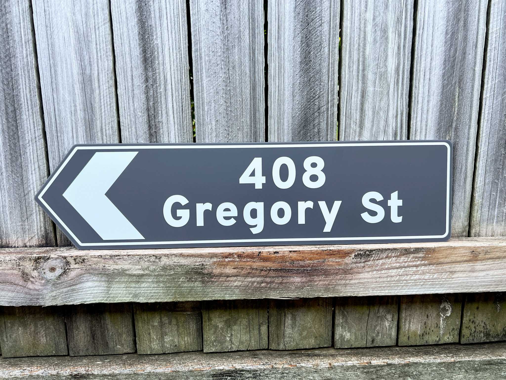 Street sign pointing to 408 Gregory St against a wooden fence background
