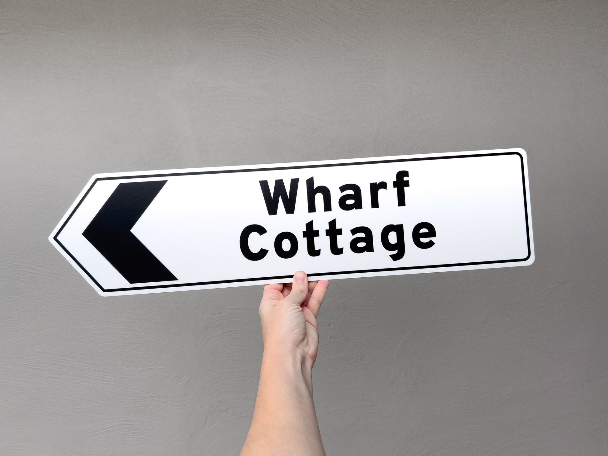 A fun novelty direction sign that reads 'Wharf Cottage' in white and black.