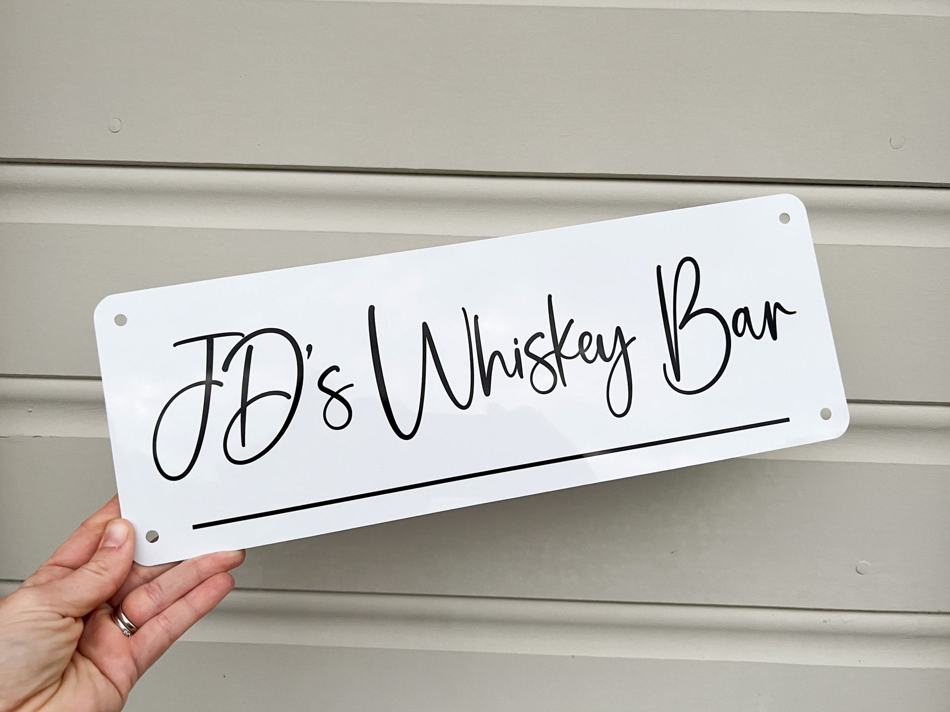 Hand holding a white sign with 'JD's Whiskey Bar' text against a neutral background