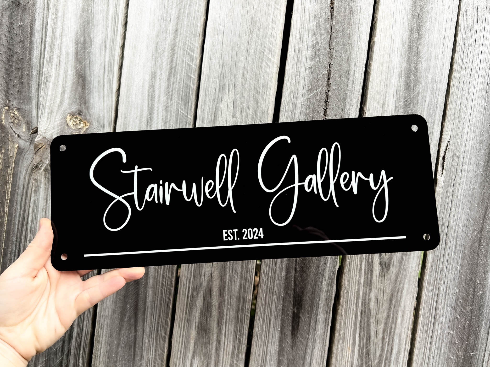 Personalised Black bar style sign with 'Stairwell Gallery EST. 2024' text held against a wooden background