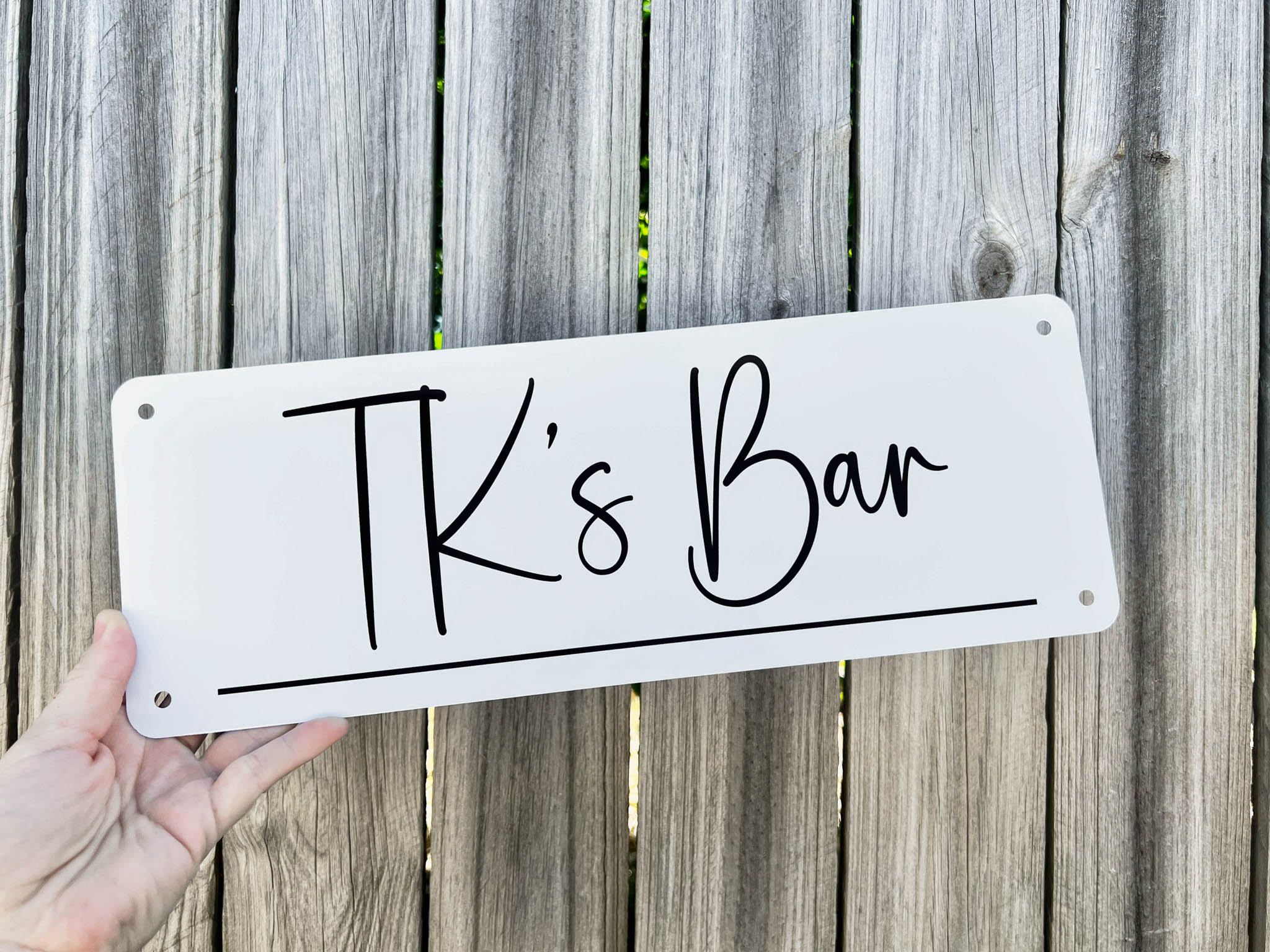 A custom white metal sign that says 'TK's Bar' in black writing.