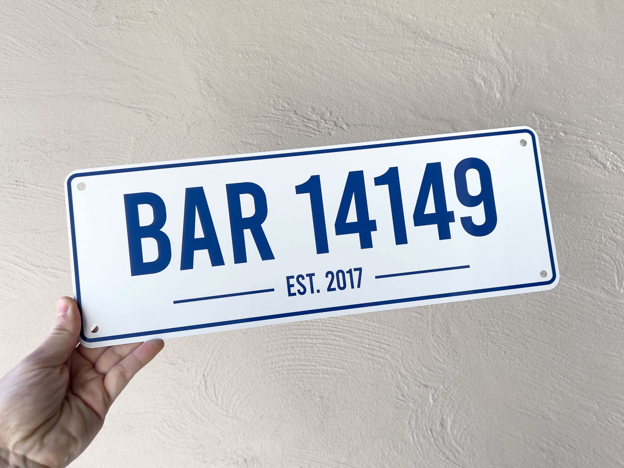 Hand holding a custom printed bar sign with 'BAR 14149 EST. 2017' on a plain background