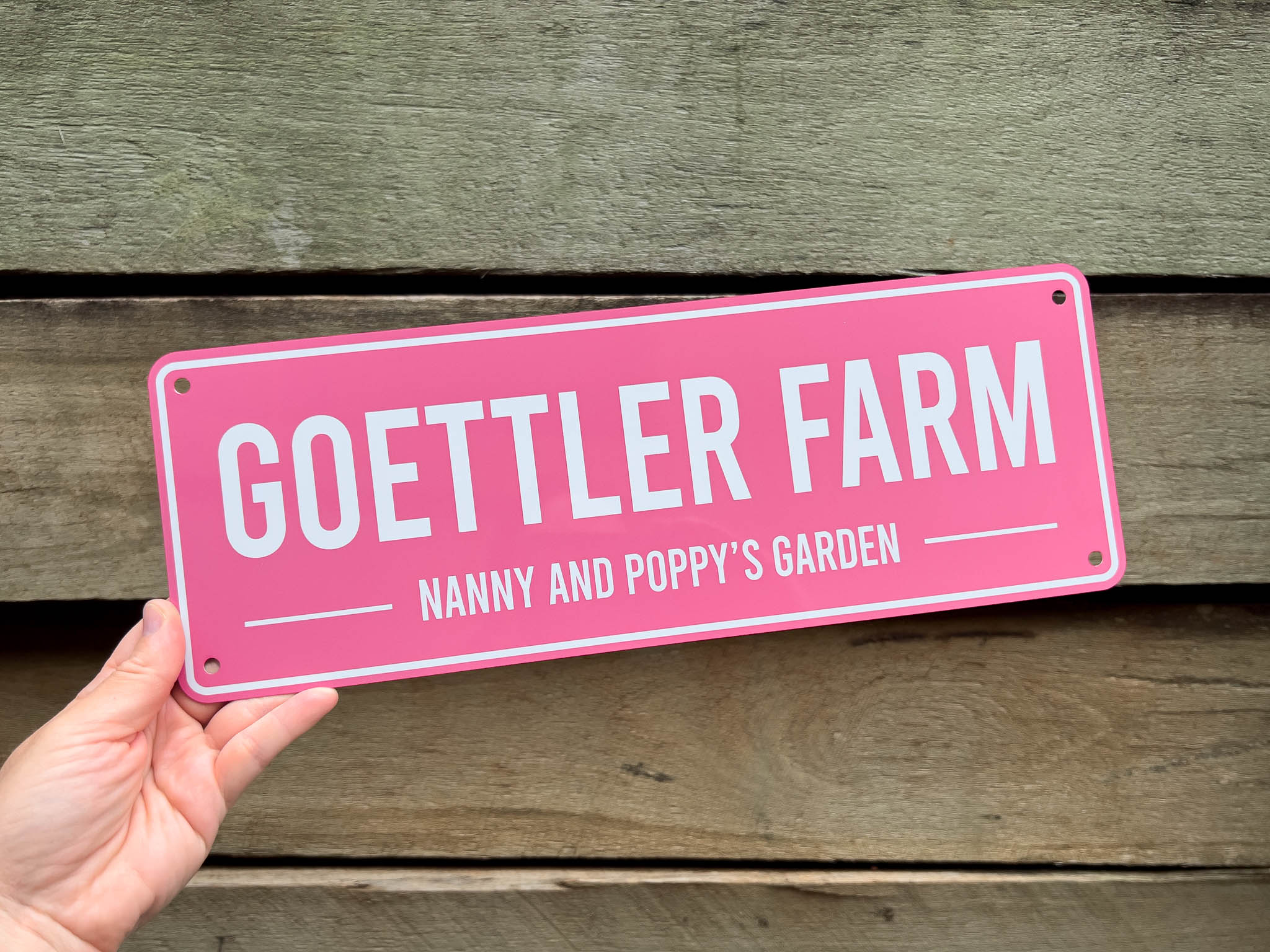 Pink bar style sign with 'Goettler Farm' text held against a wooden background