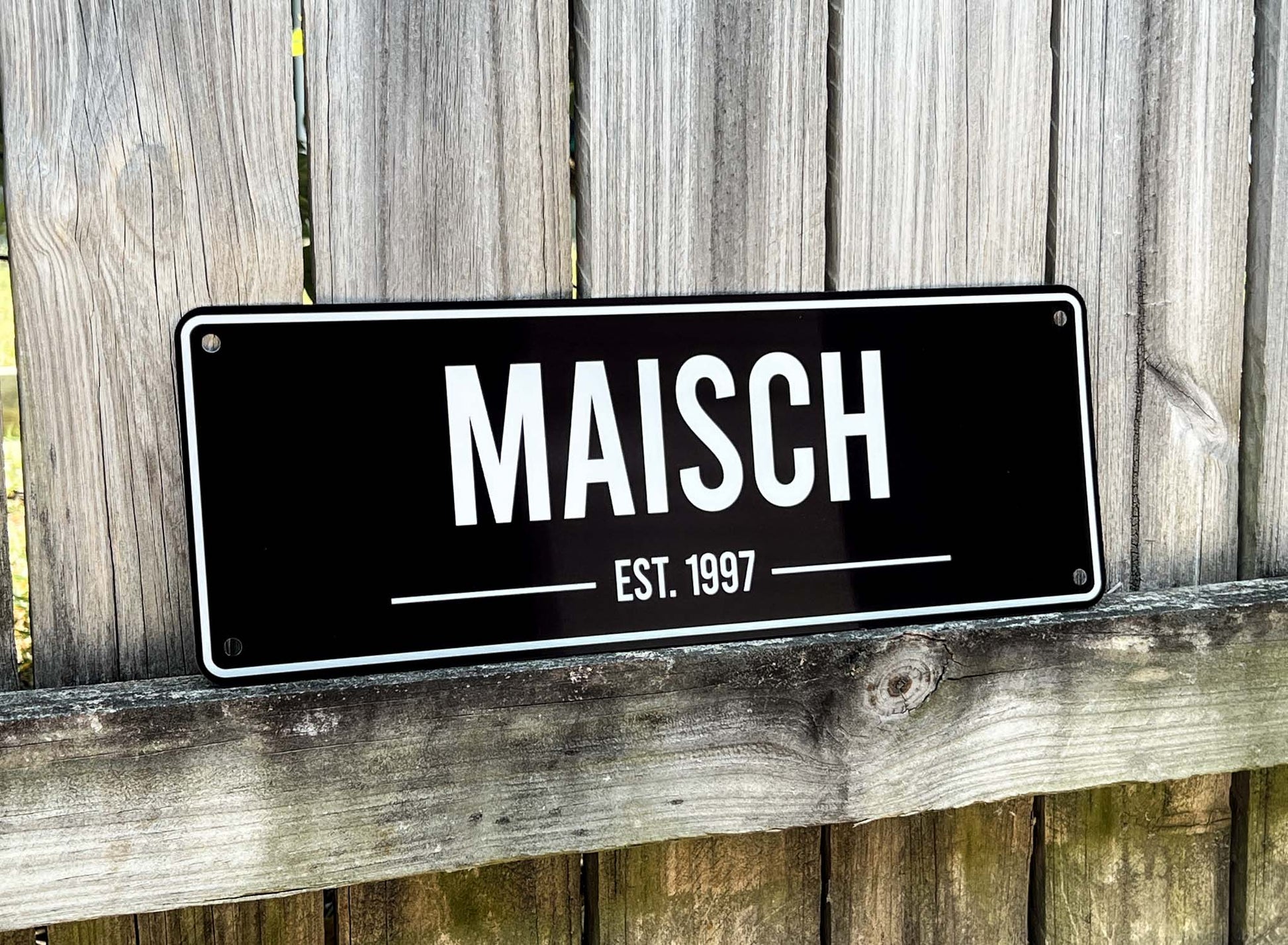 Black bar style sign with 'MAISCH EST. 1997' text on a wooden background