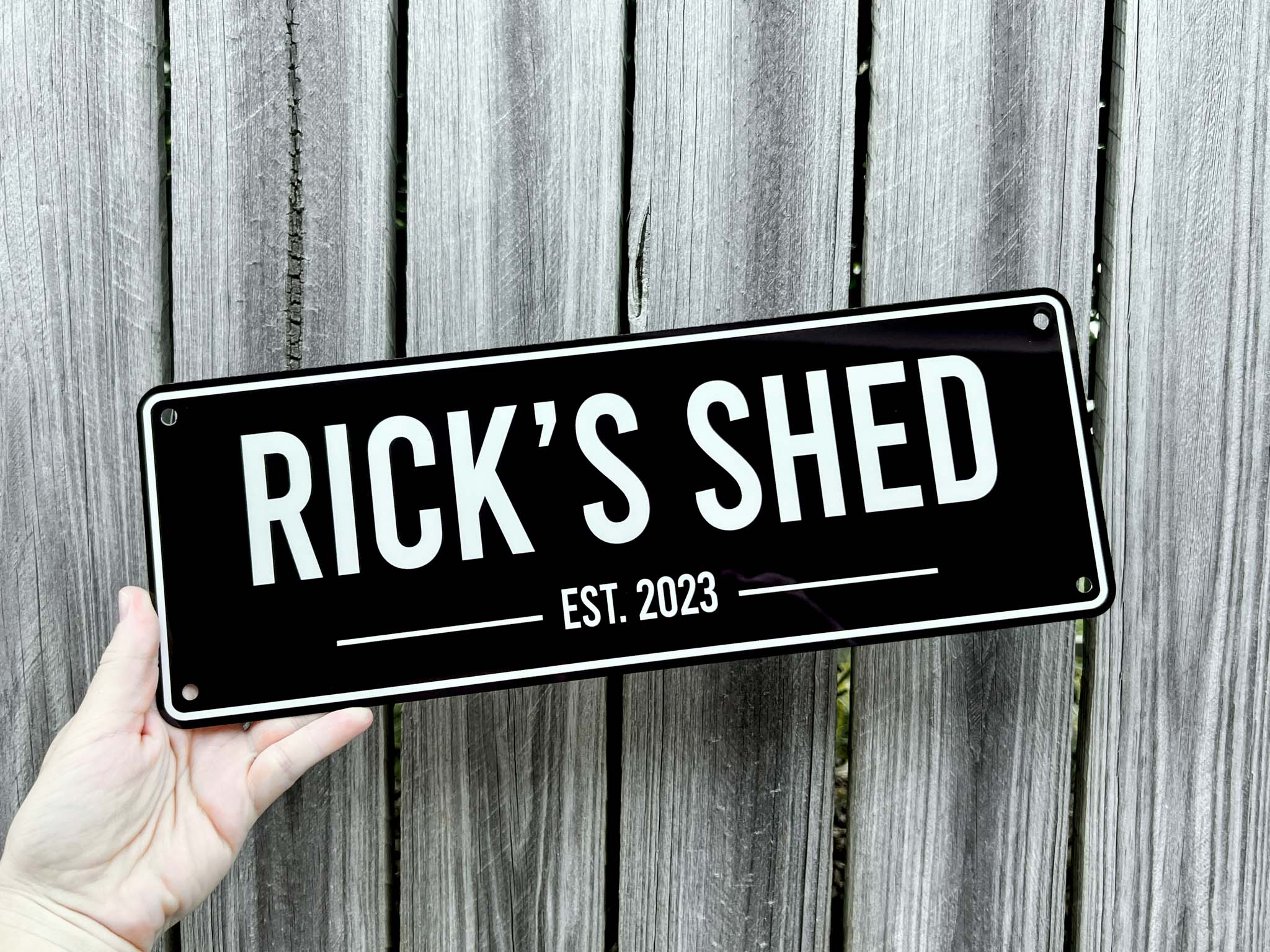 A custom printed bar style sign that says 'Rick's Shed Est. 2023' against a wooden background