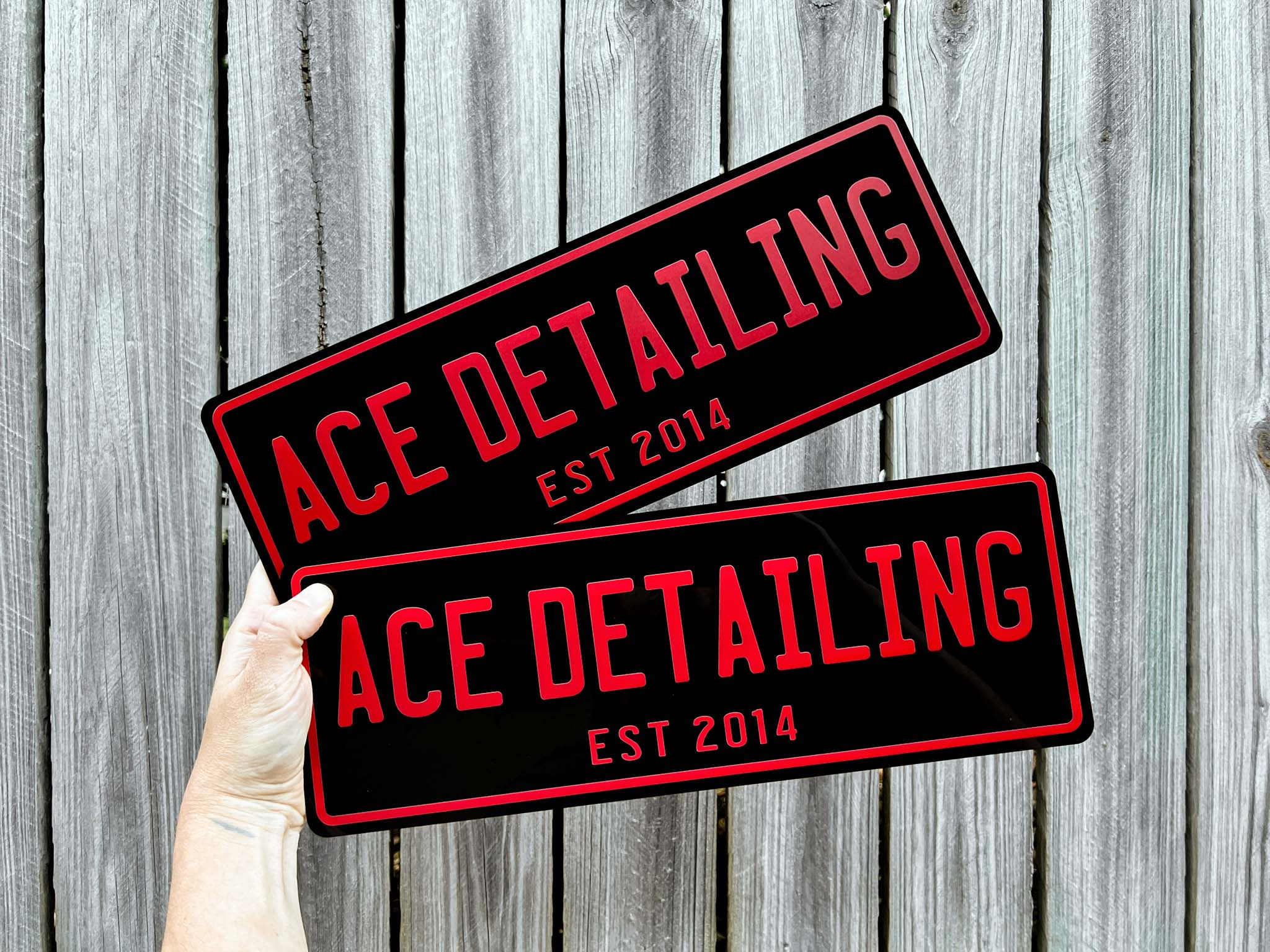 Two 'Ace Detailing' acrylic plates in black and red held against a wooden background